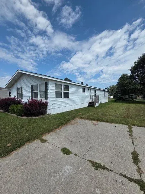 White single-story house with green lawn, driveway, and blue sky with clouds.
