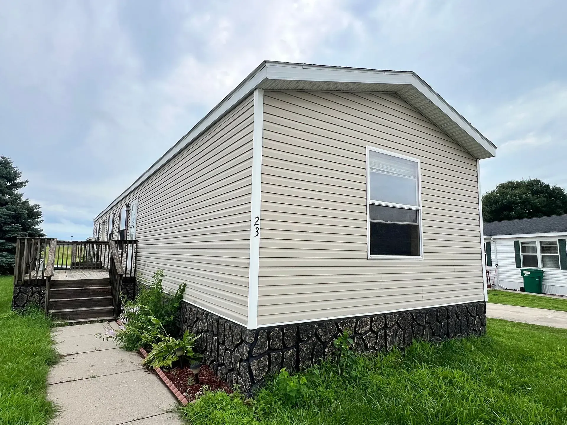 Tan mobile home with steps and a window, against a cloudy sky.