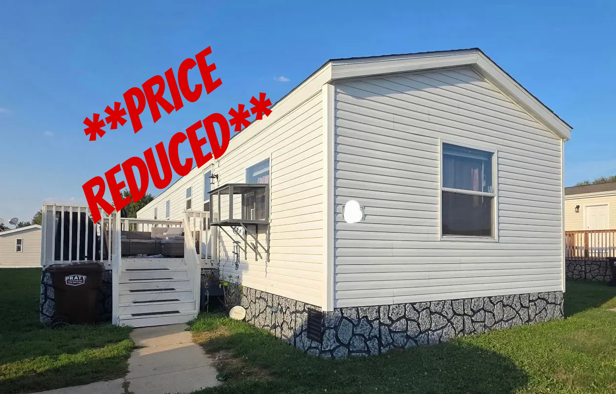 White mobile home with stone-look skirting and wooden stairs leading to a deck.