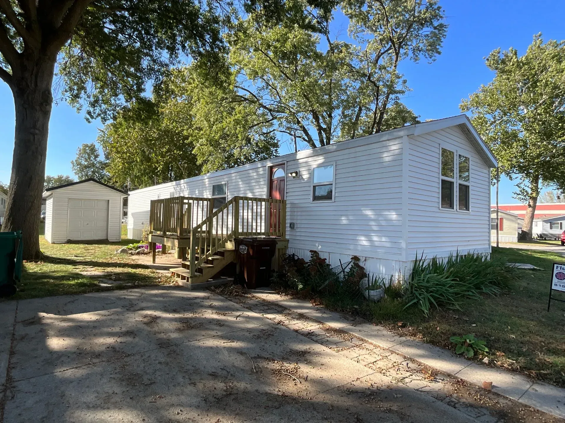 White house with wooden porch and shed on a sunny day.