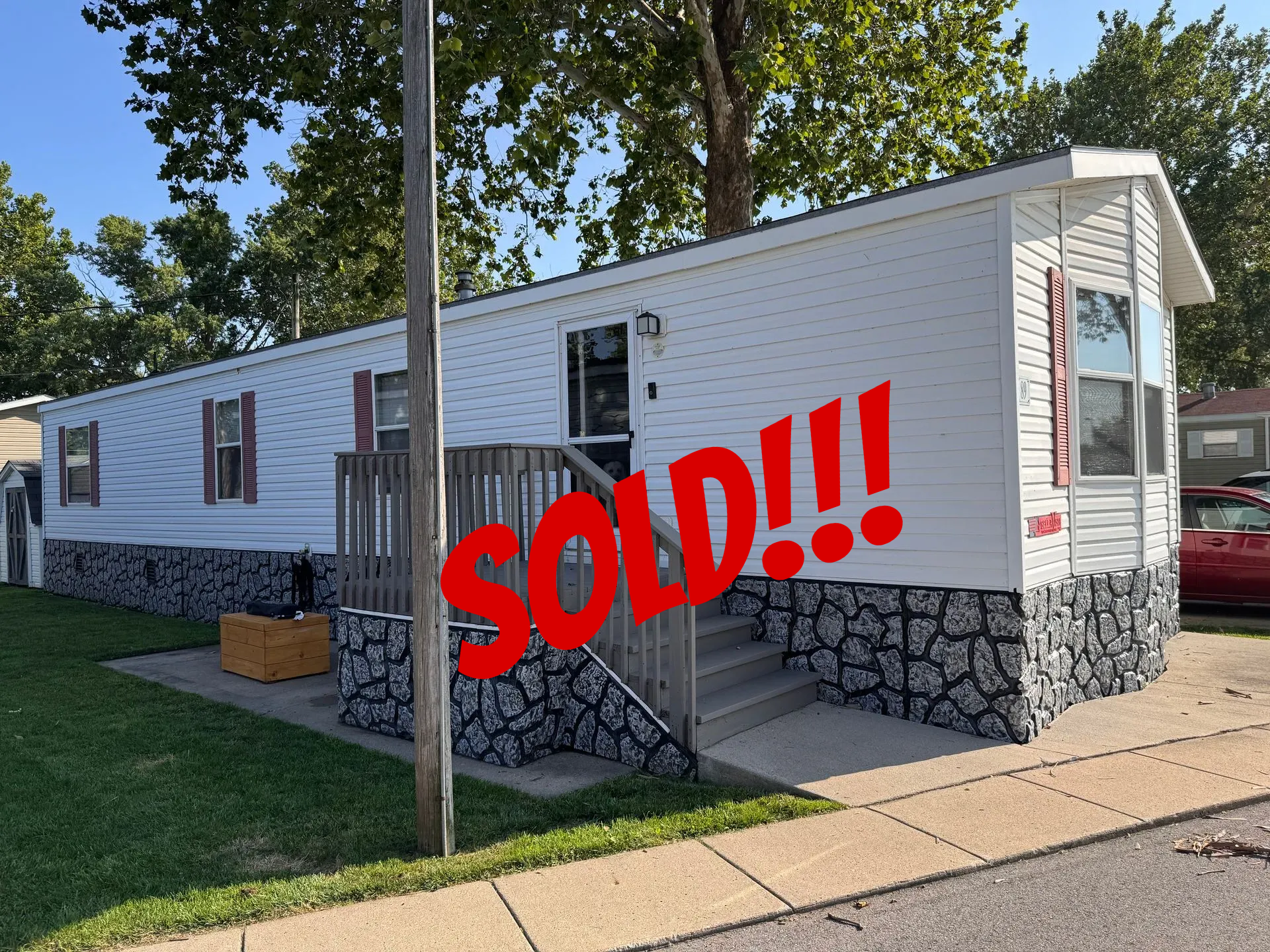 White mobile home with stone-patterned skirting and wooden steps leading to the front door.