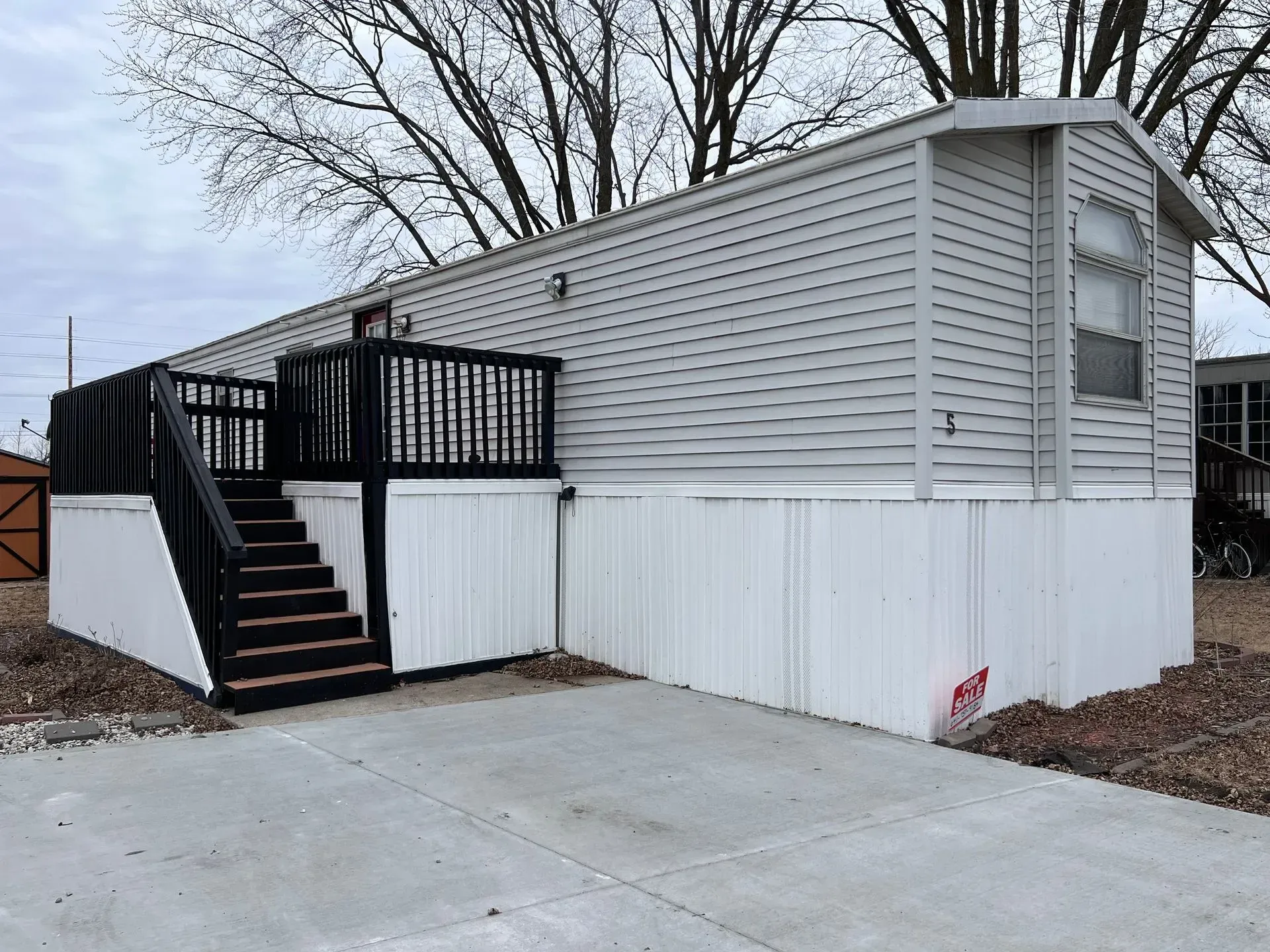 Mobile home with a gray exterior, black deck, and concrete driveway.