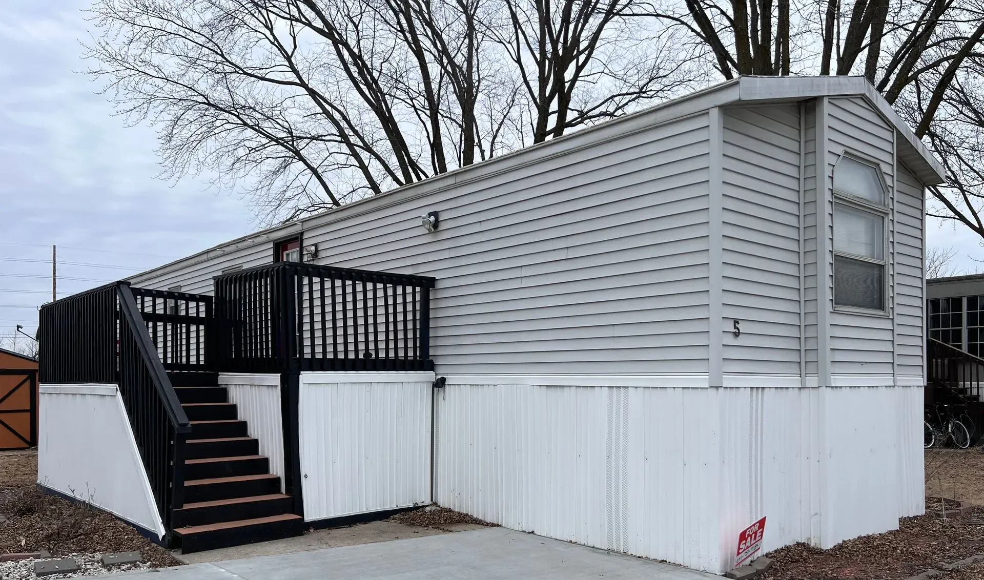 Mobile home with white and gray siding, black deck and stairs, concrete driveway.