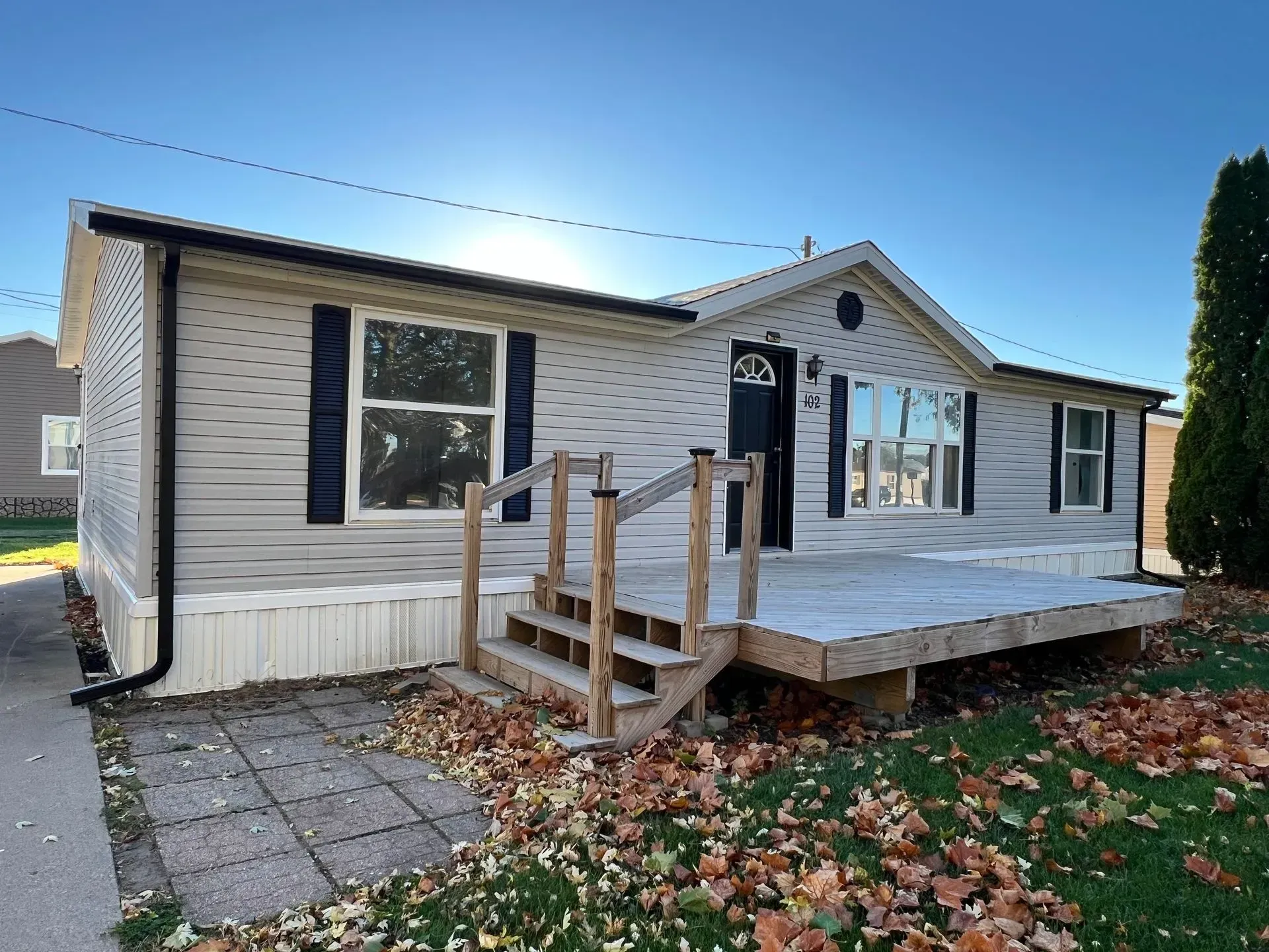 Gray and white house with a porch and steps, fallen leaves on the ground.