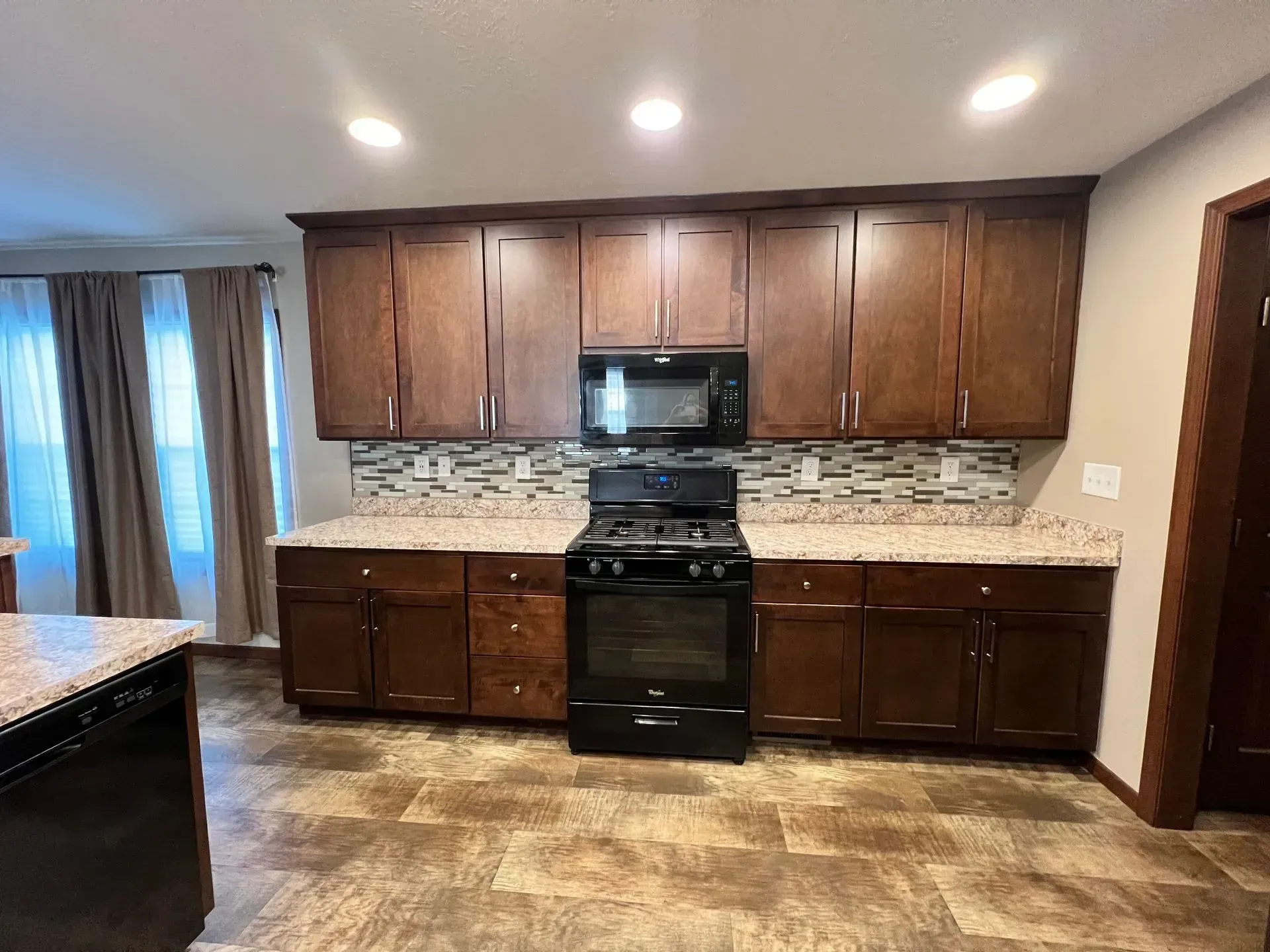 Kitchen with dark wood cabinets, black appliances, and speckled countertops.