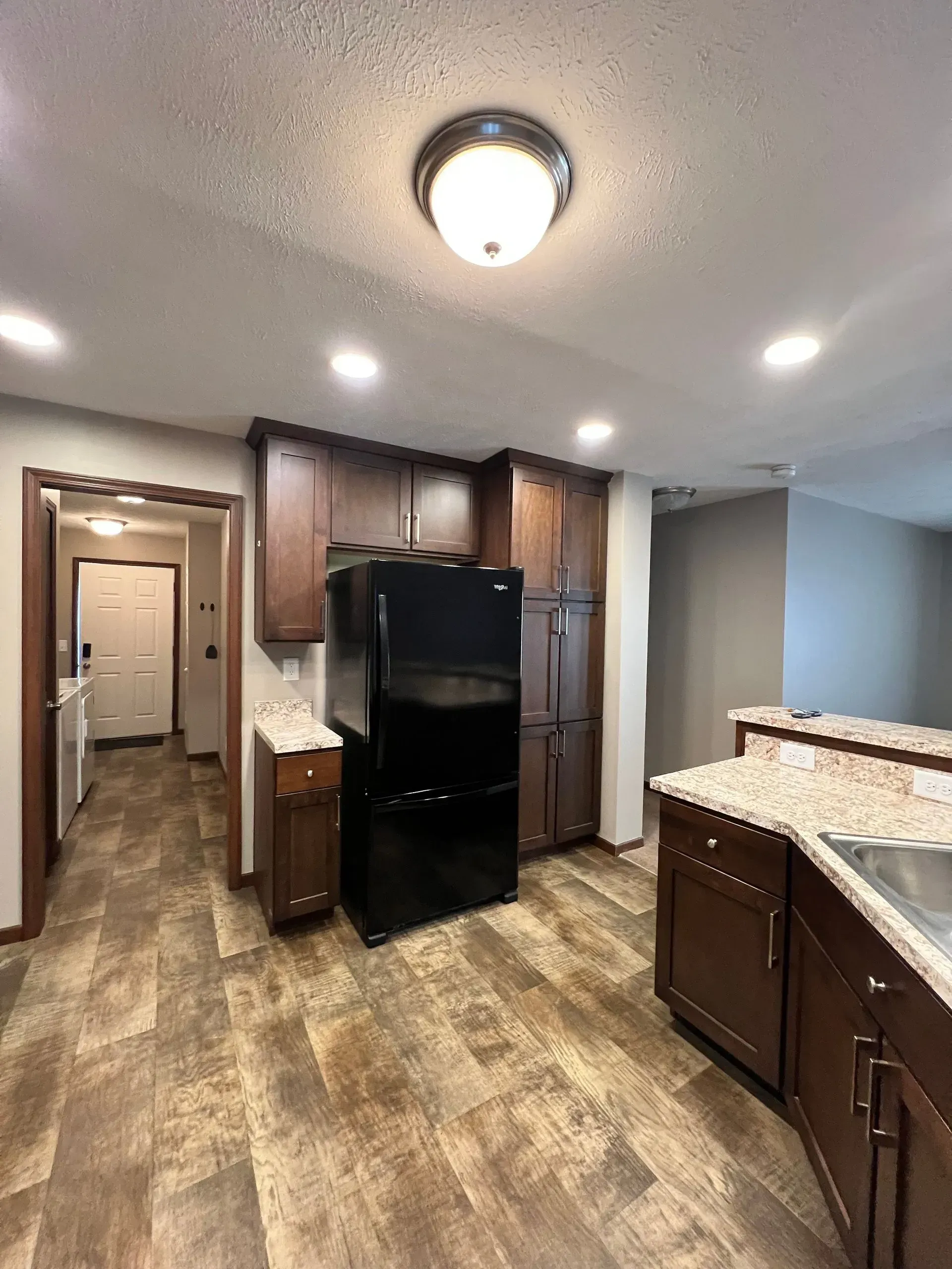 Kitchen with dark wood cabinets, black refrigerator, and wood-look flooring.