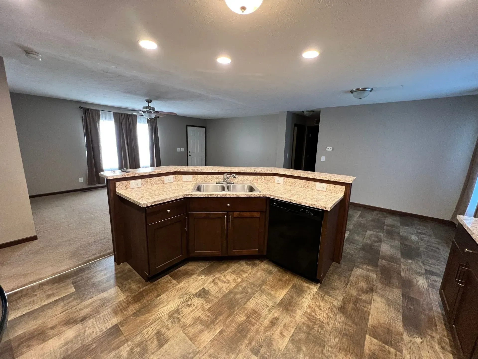 Kitchen island with sink and cabinets, open to living room. Brown and tan tones.