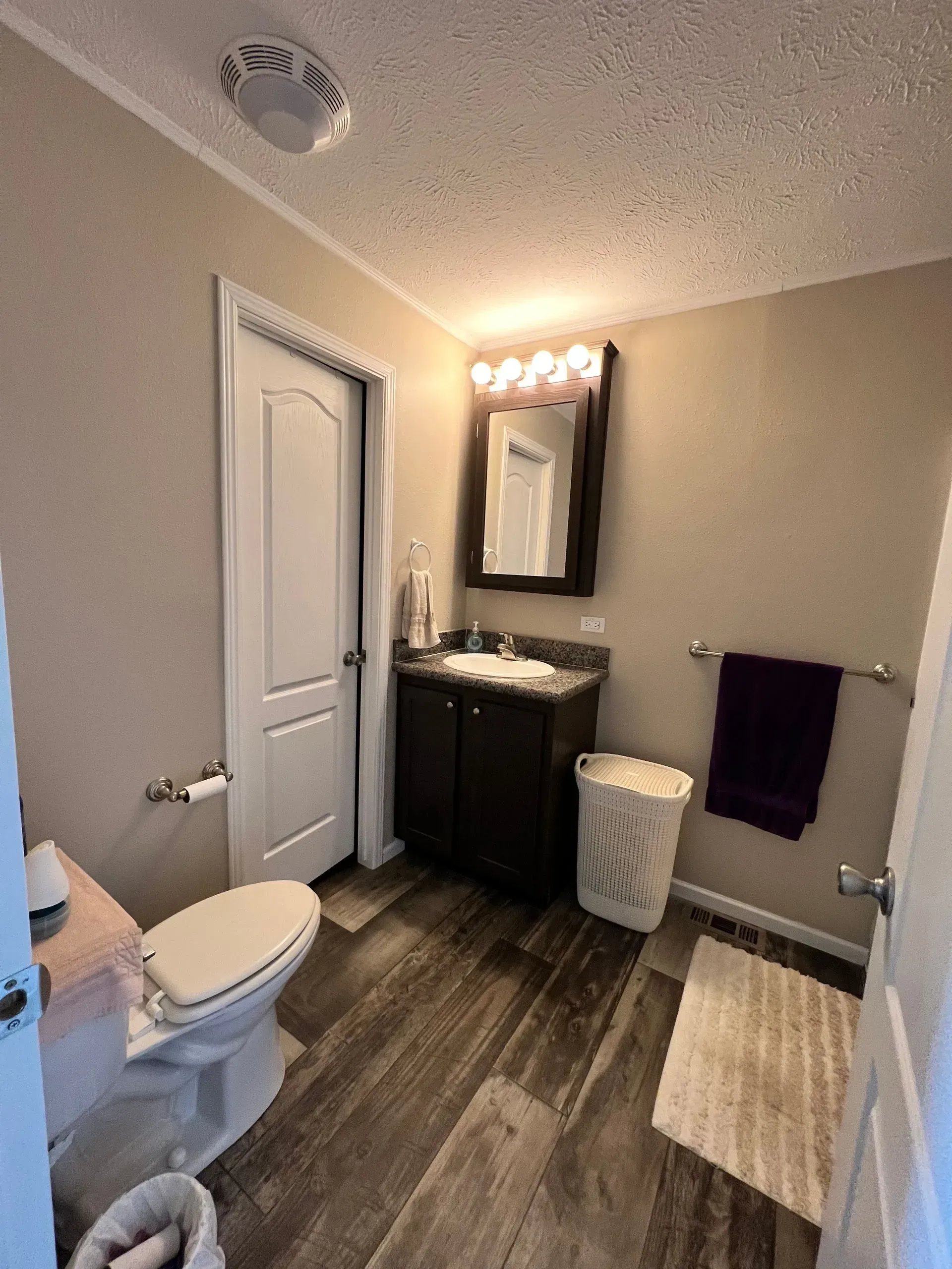 Bathroom with dark brown vanity, toilet, and wood-look floor. White door and beige walls.