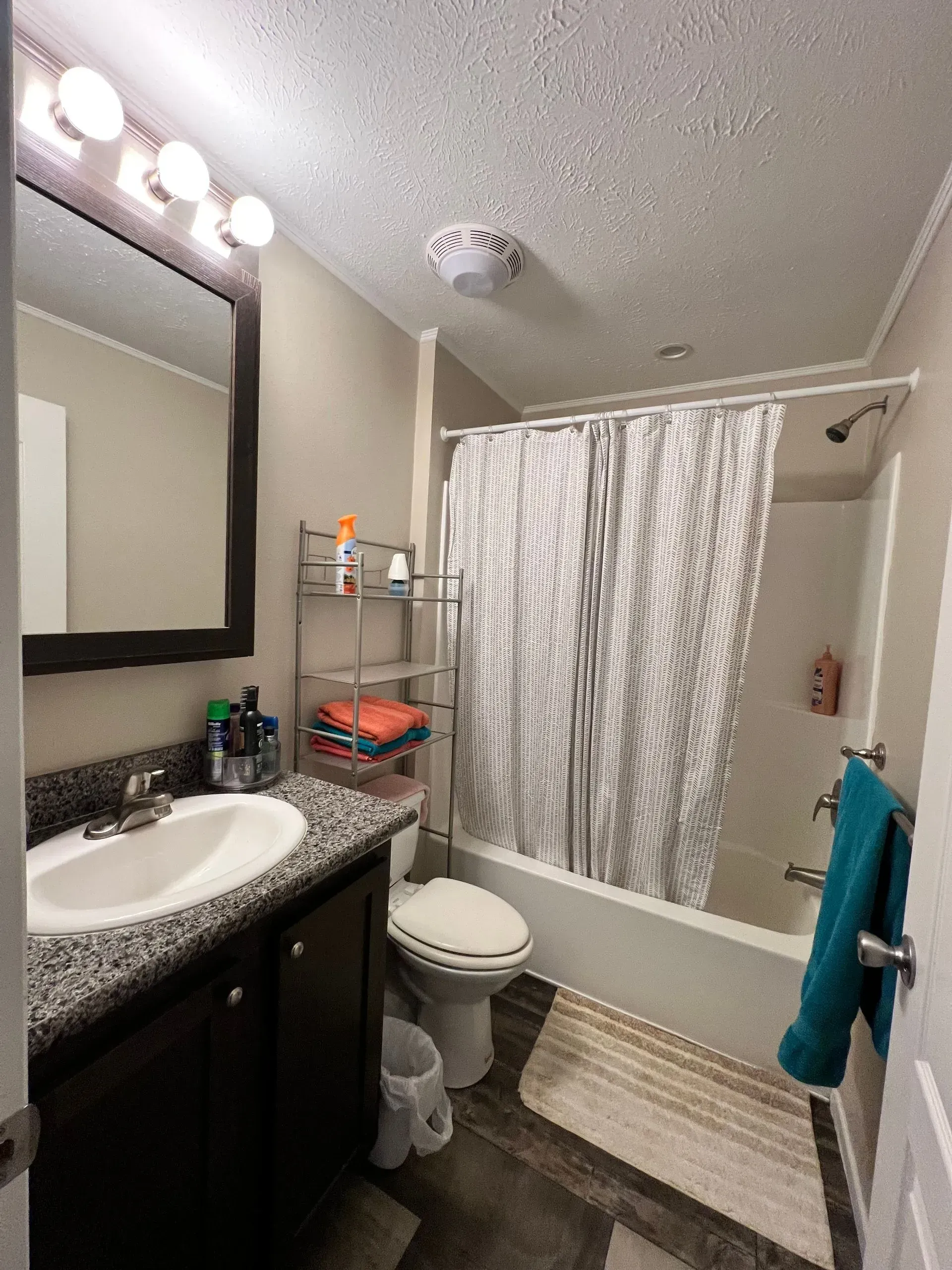 Bathroom with dark vanity, white fixtures, shower with patterned curtain, and towel on door.