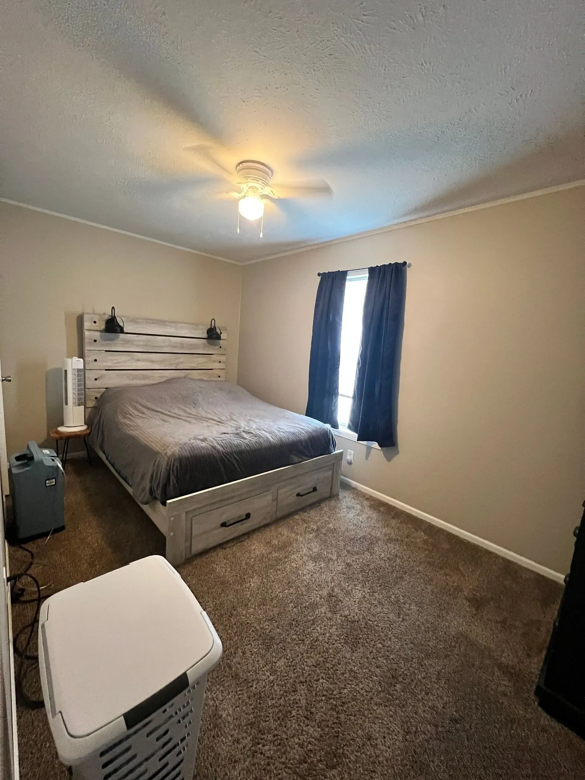 Bedroom with a bed, dresser, and a window with dark curtains. Brown carpet.