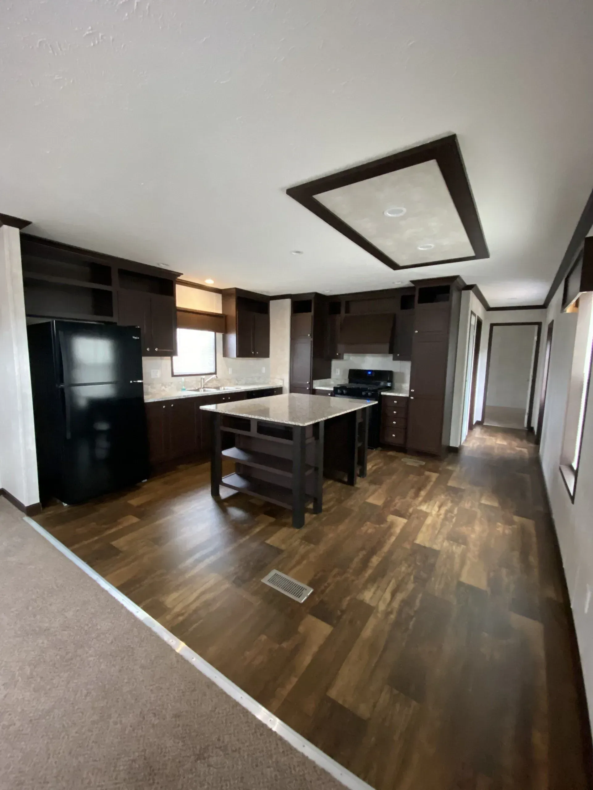 Modern kitchen with dark cabinetry, black refrigerator, and an island with open shelving. Dark wood floors.