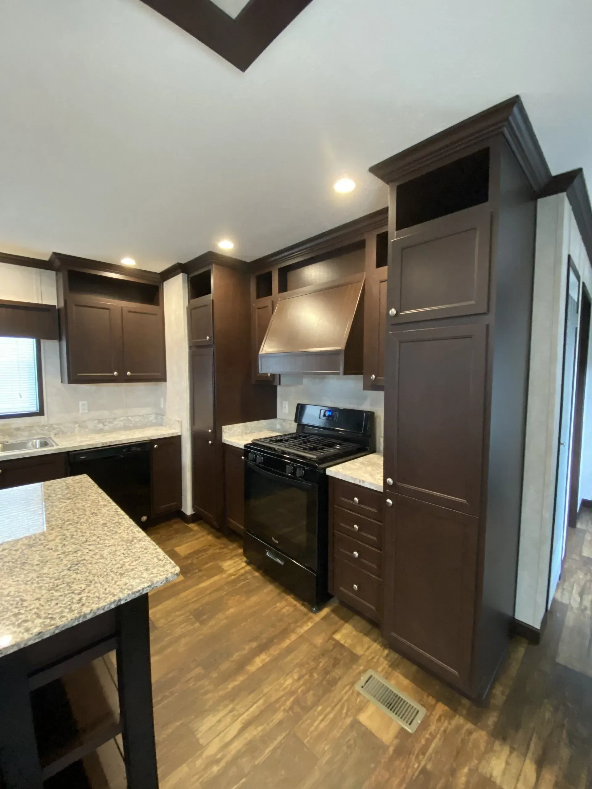 Dark brown kitchen with black appliances, white countertops, and wood floors.