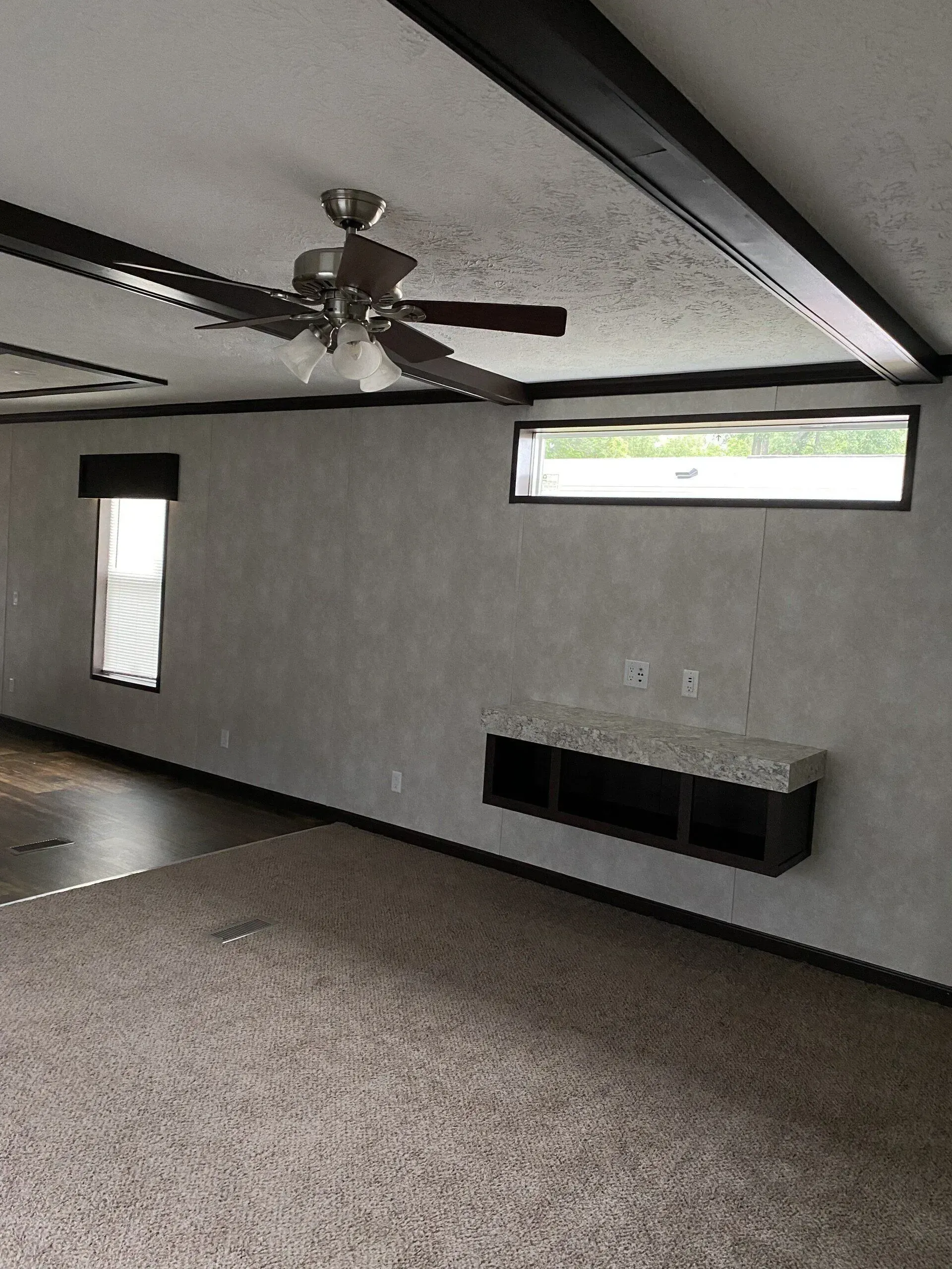 Interior of a room with a ceiling fan, windows, carpet, and a built-in shelf.
