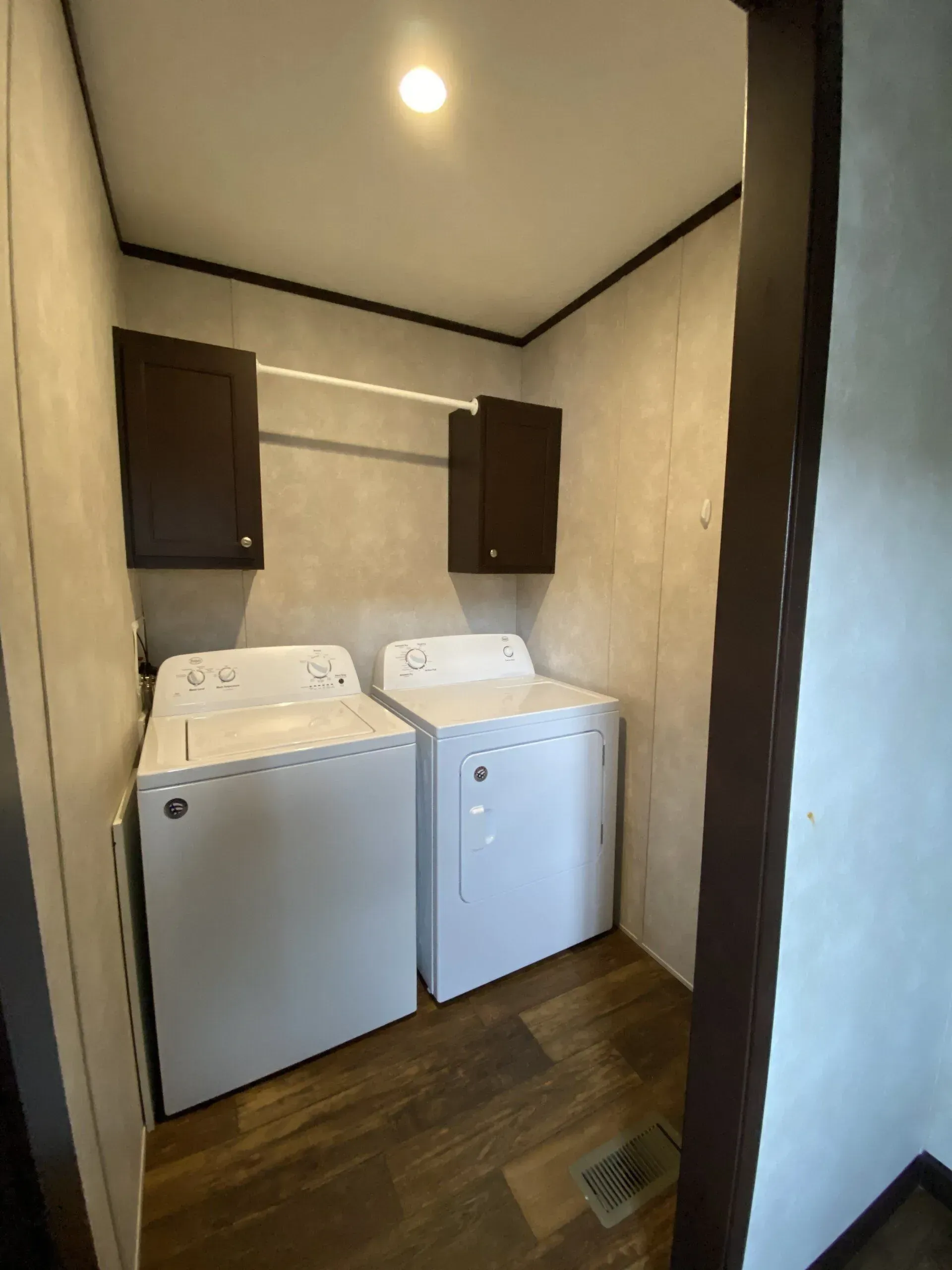 Laundry room with white washer and dryer, brown cabinets, and a hanging rod.