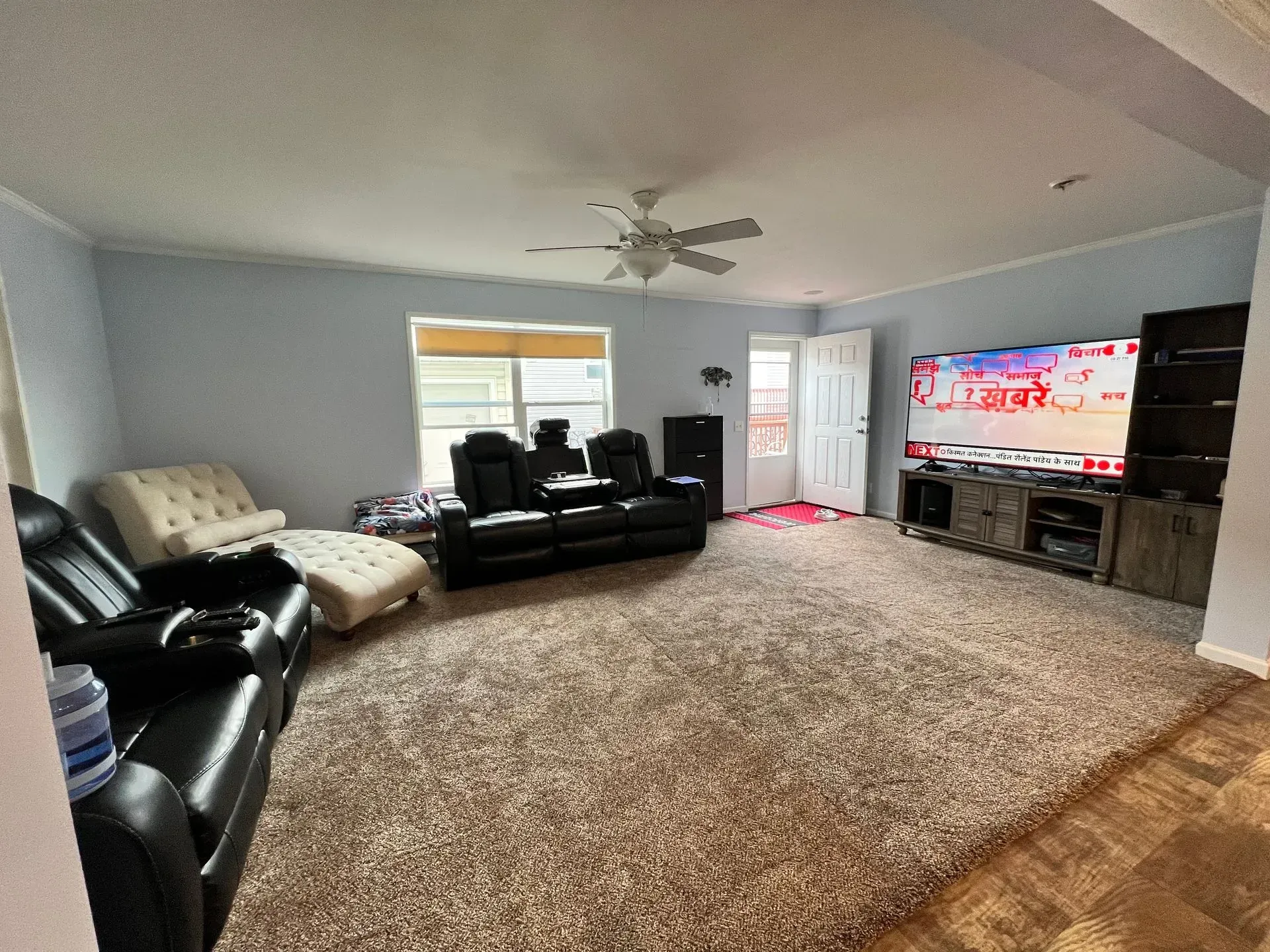 Living room with brown carpet, blue walls, a black leather sofa, and a large TV.