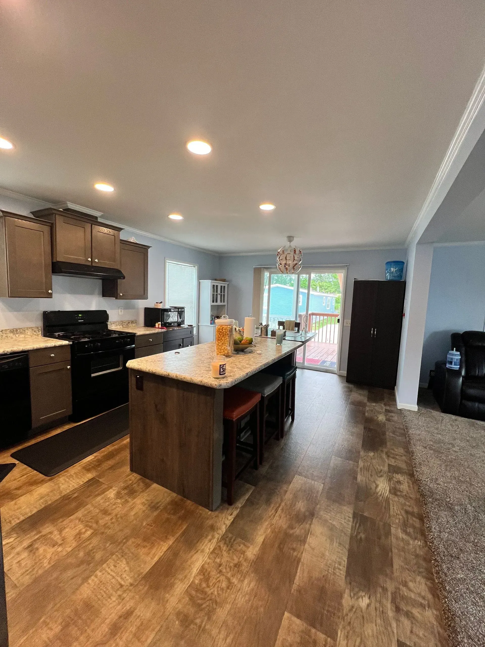 Kitchen with island, dark cabinets, appliances, and wooden flooring. Sliding door leads to a deck.