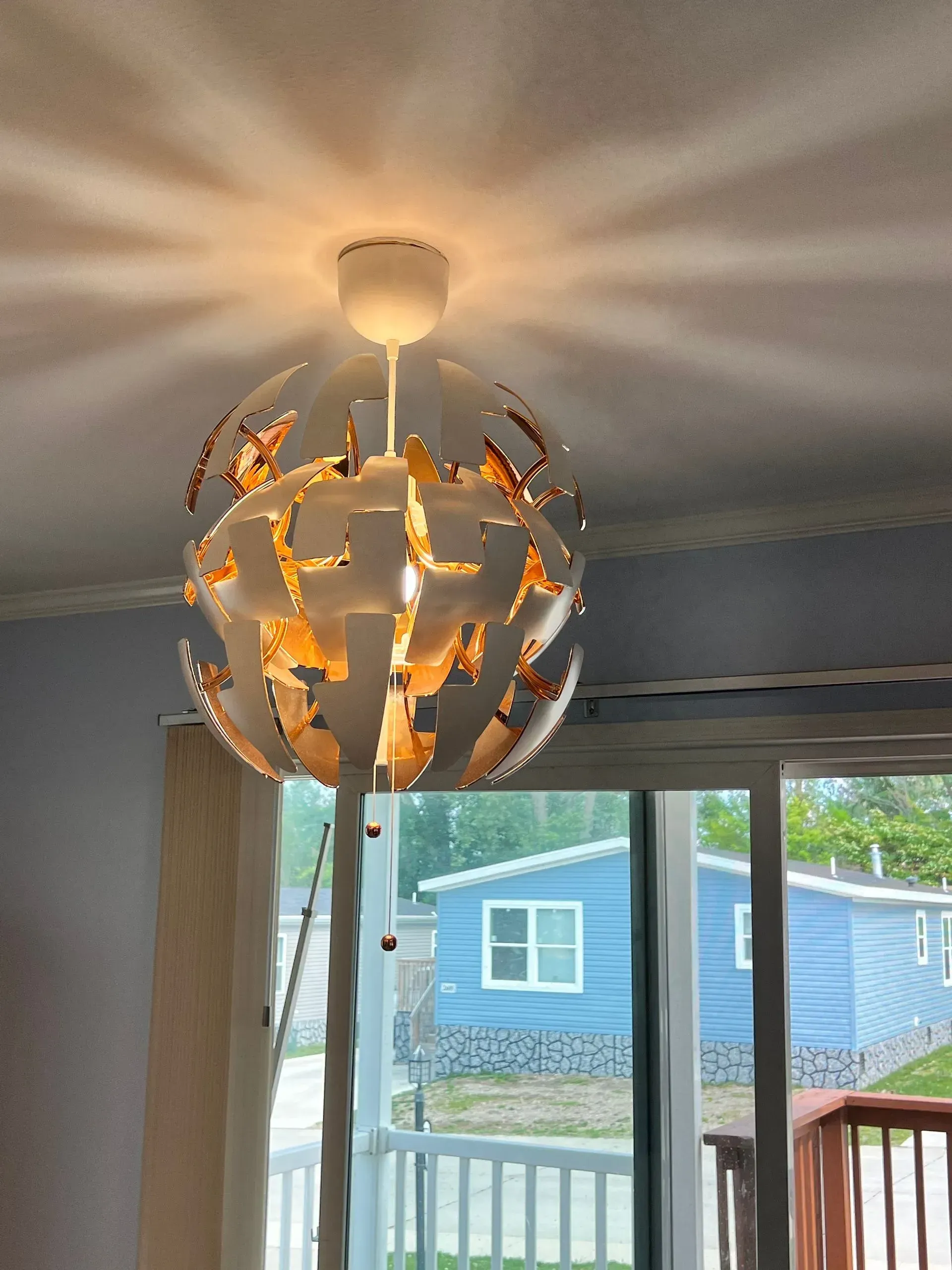 White globe pendant lamp illuminates a room, with sunlight shining through a window onto a blue house.