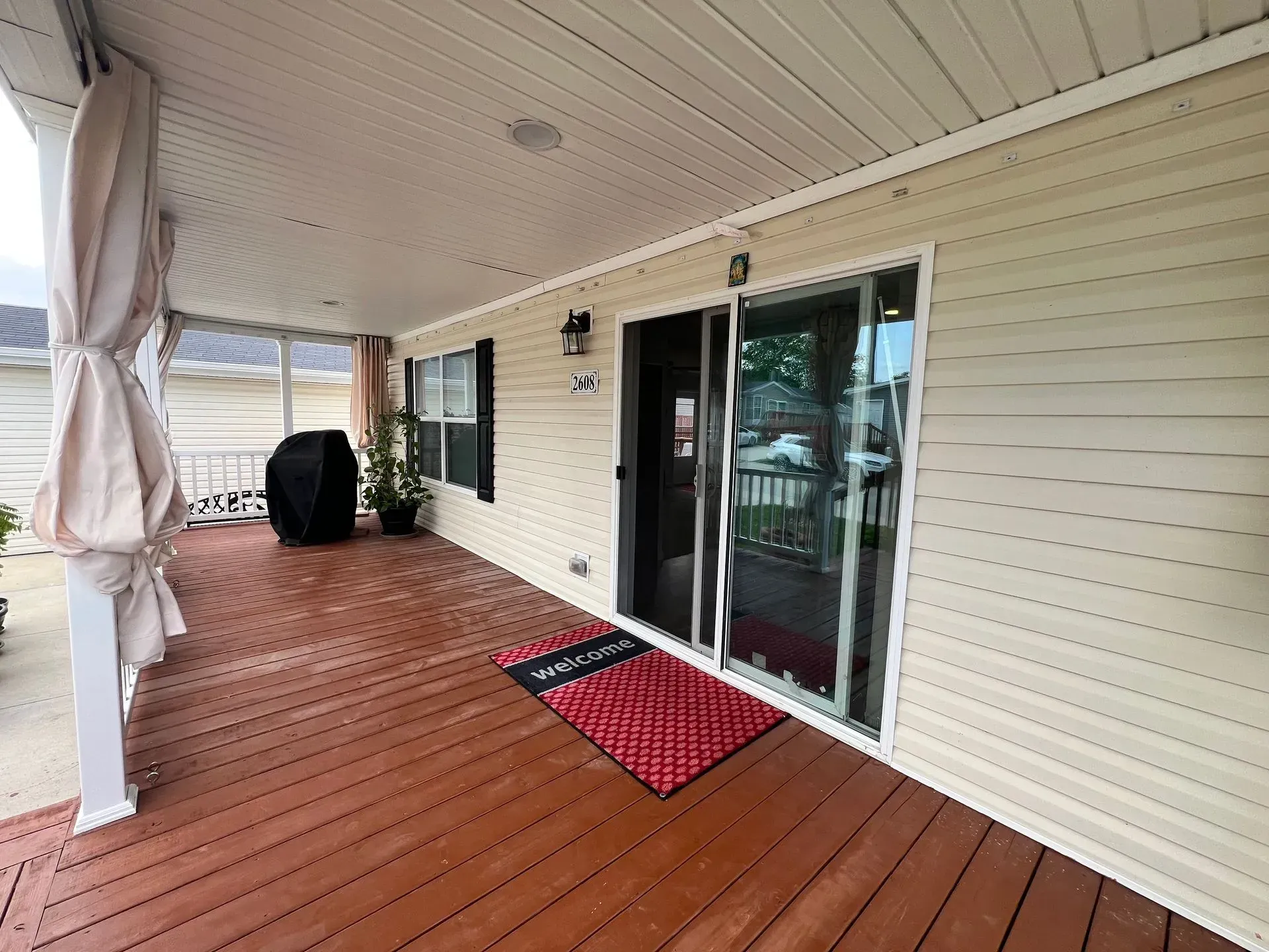 Covered wooden porch with sliding glass door and welcome mat.