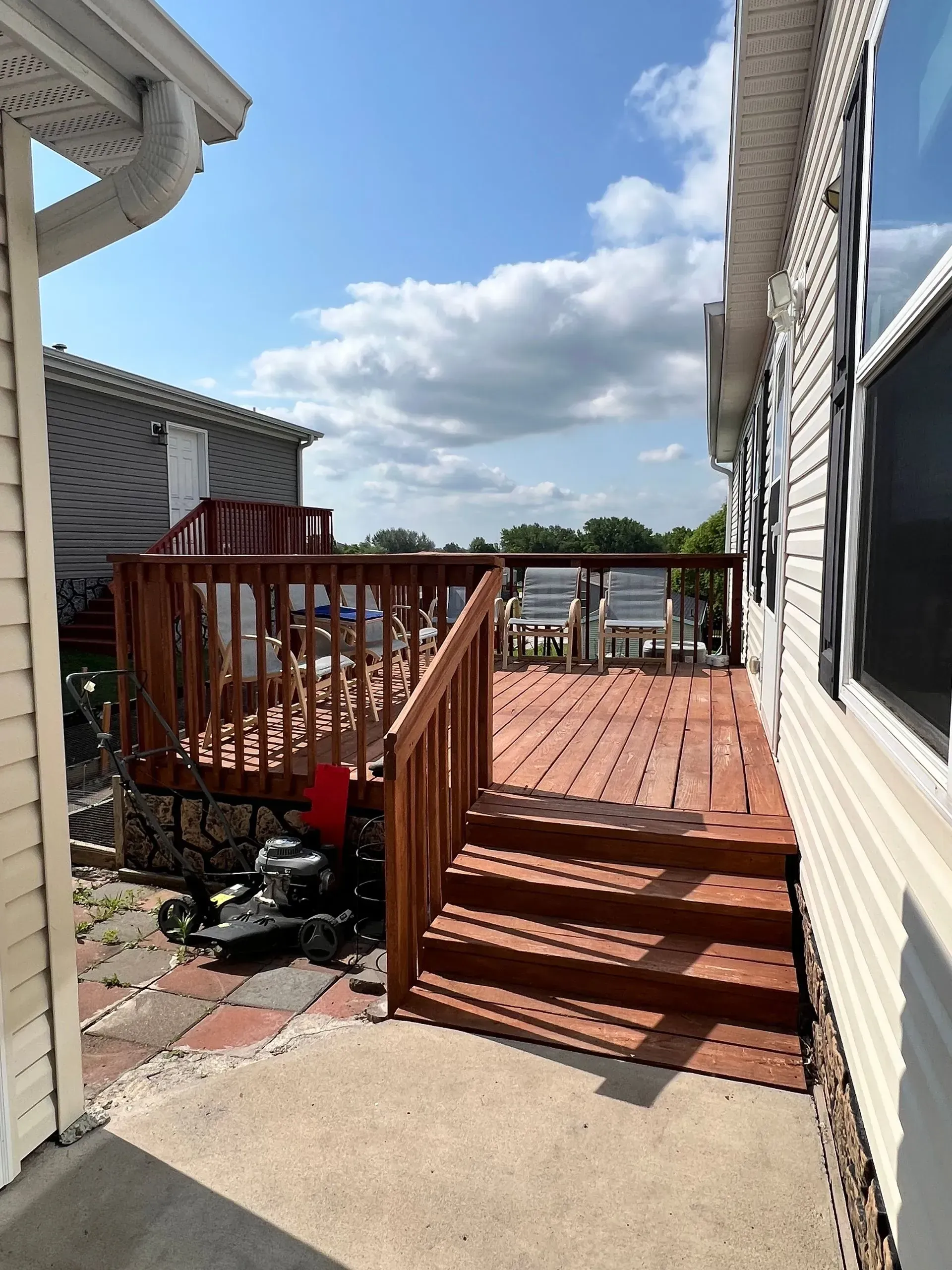 Wooden deck attached to a house with stairs, view of another building, blue sky with clouds.