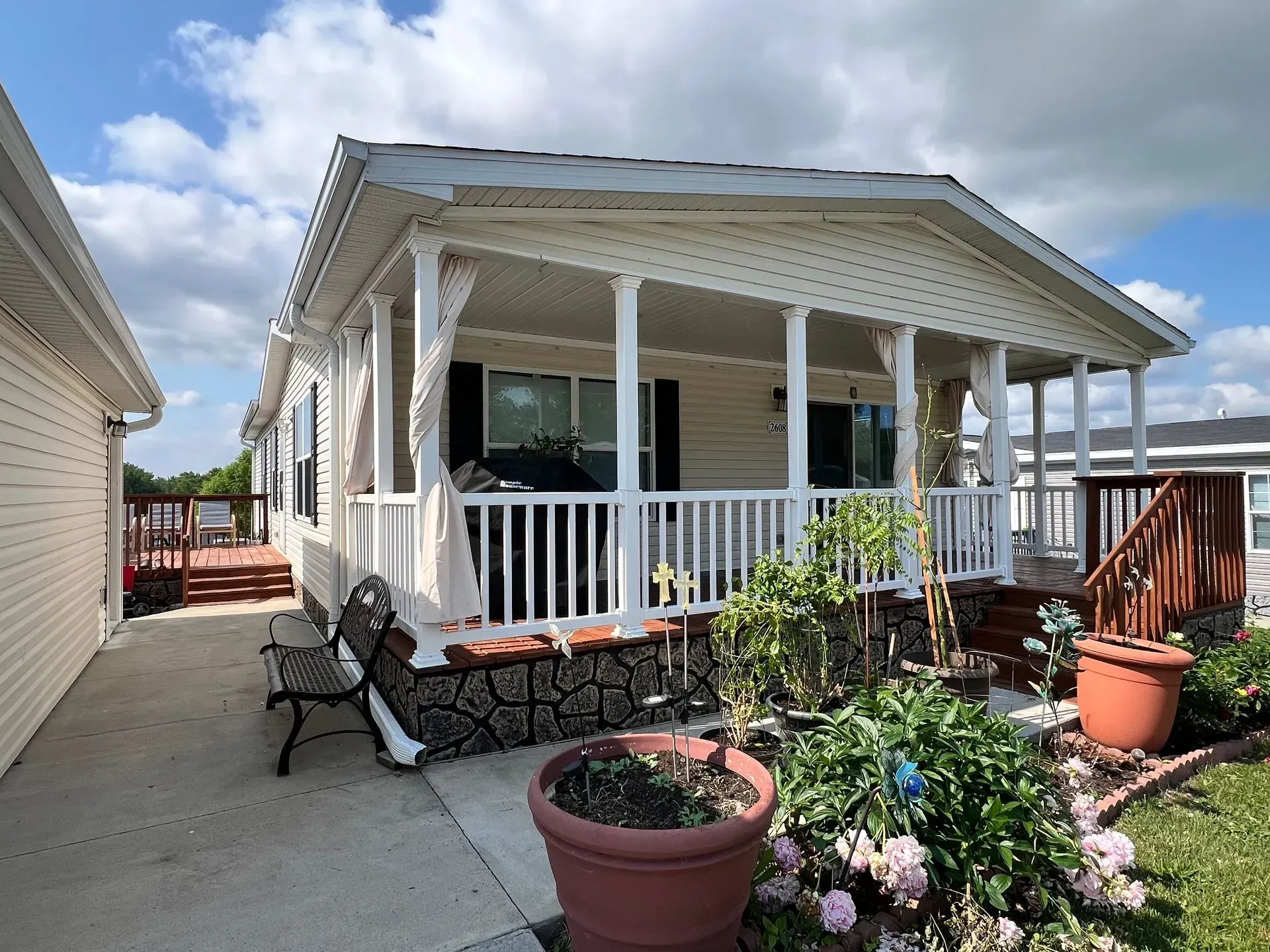 Mobile home with porch, white siding, and garden in front. A black bench sits by the porch.