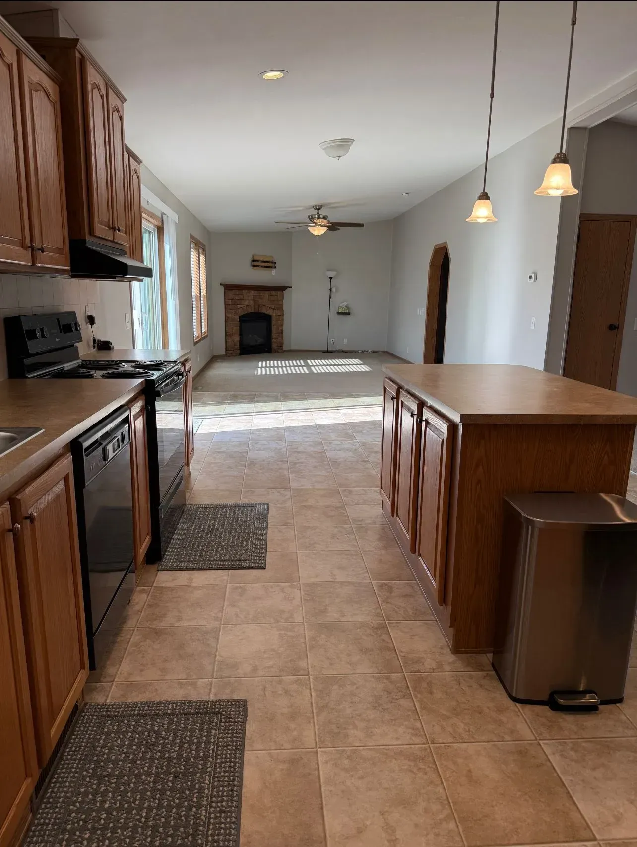 Kitchen with brown cabinets, island, and tile floor, leading to a living room with a fireplace.