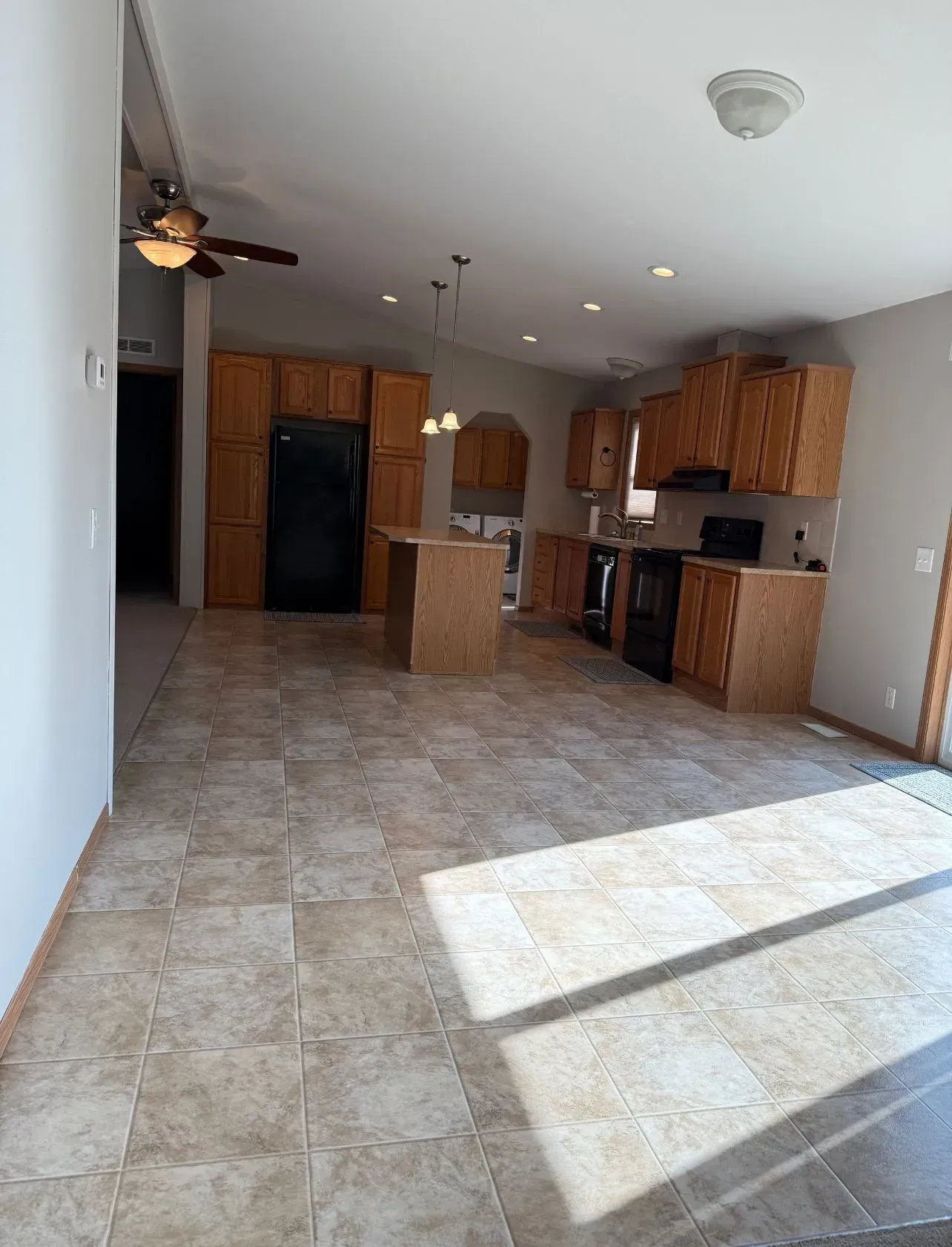 Open-concept kitchen with tile floor, wood cabinets, and black appliances.