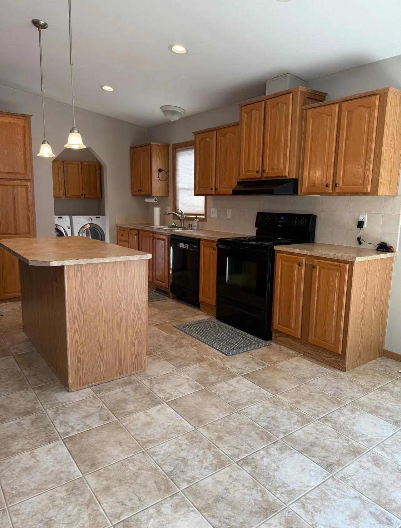 Kitchen with wooden cabinets, black appliances, and island with light-colored flooring.