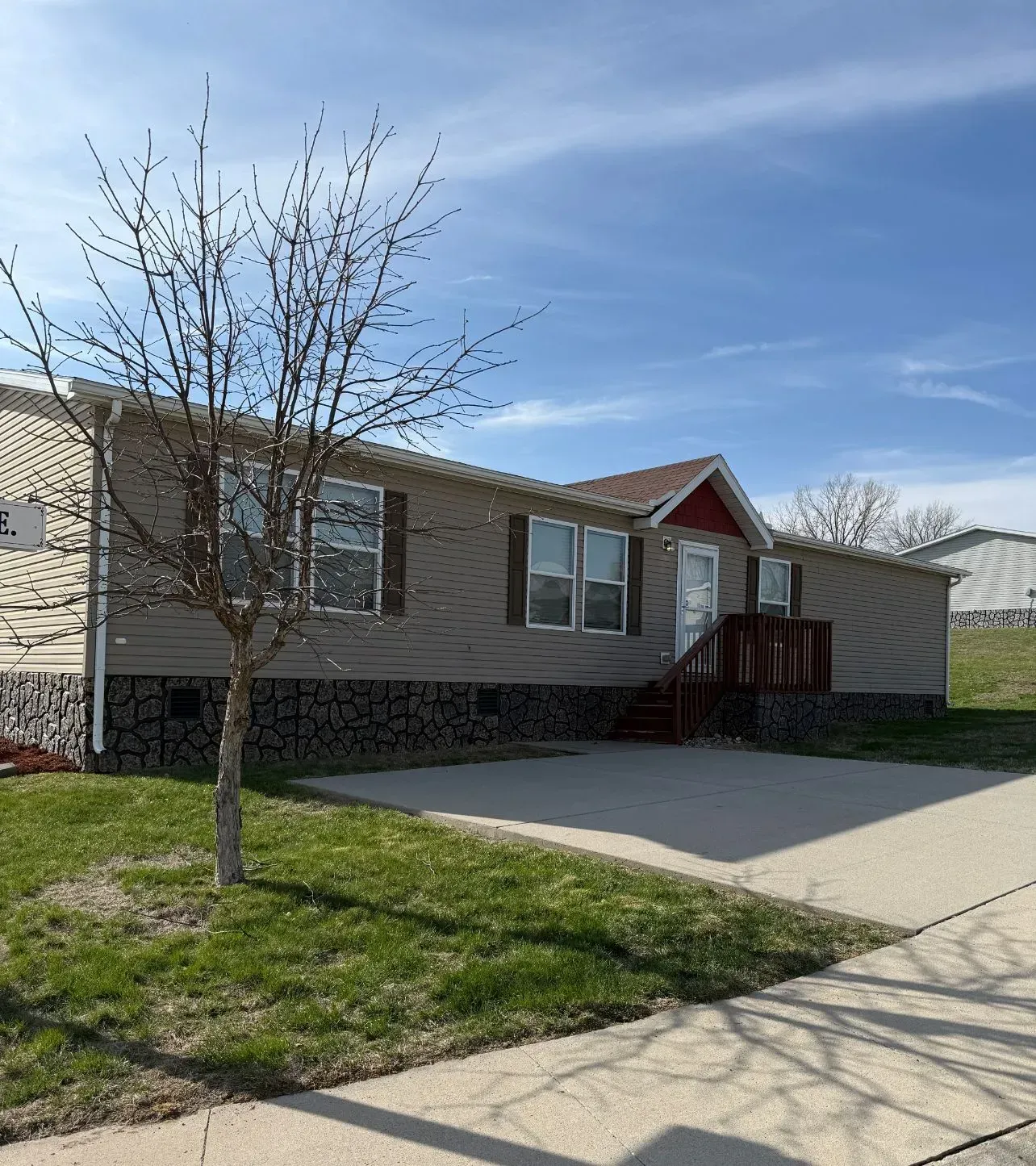 Brown-sided house with brown shutters and a red-trimmed door, set on a cement foundation and driveway under a blue sky.