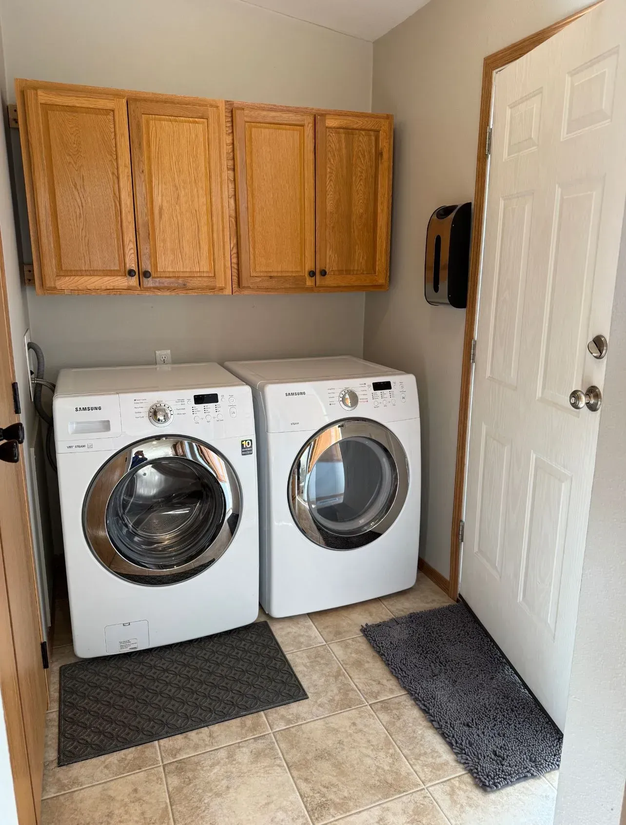 Laundry room with white washer and dryer, tan cabinets, and a white door.