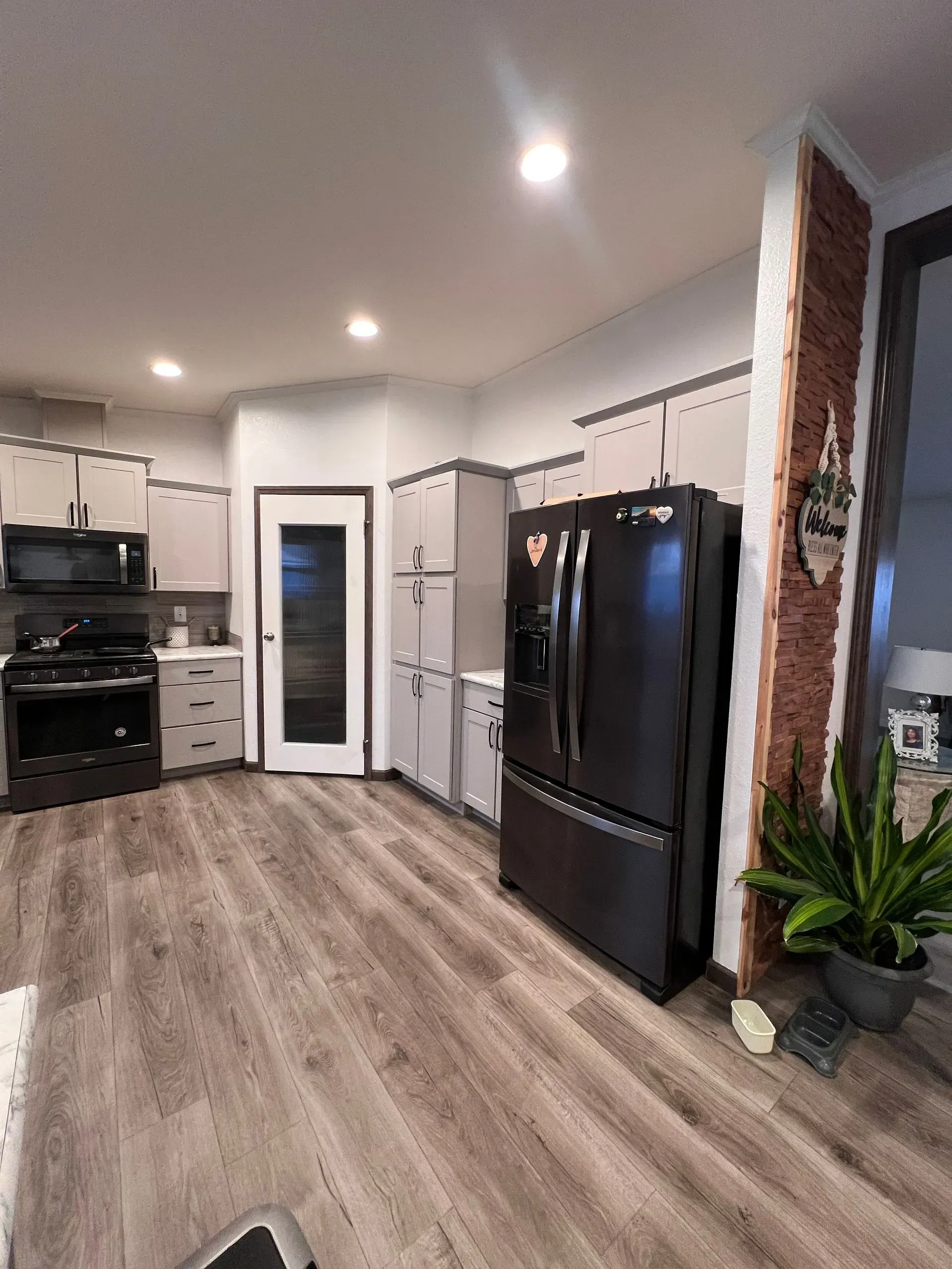 Kitchen with gray cabinets, black appliances, and wood-look flooring. A refrigerator and a brick pillar are visible.