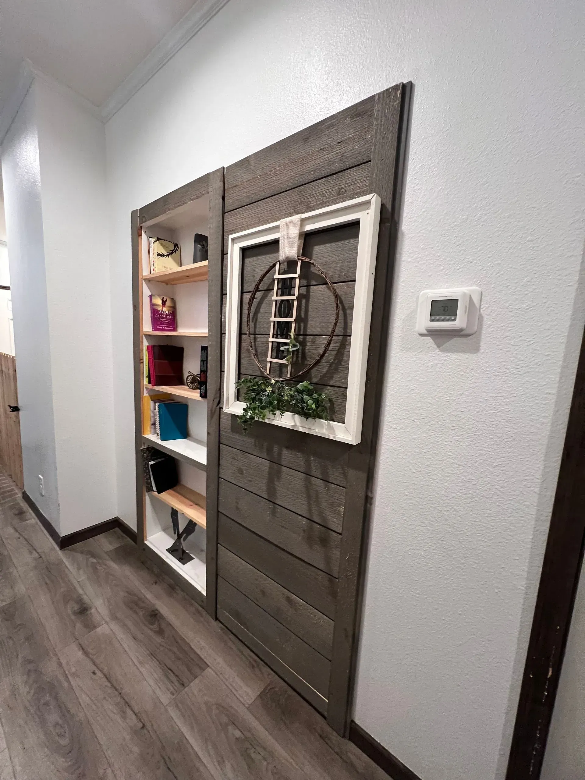 Wooden door with decorative window frame, shelf on left, wood floor.