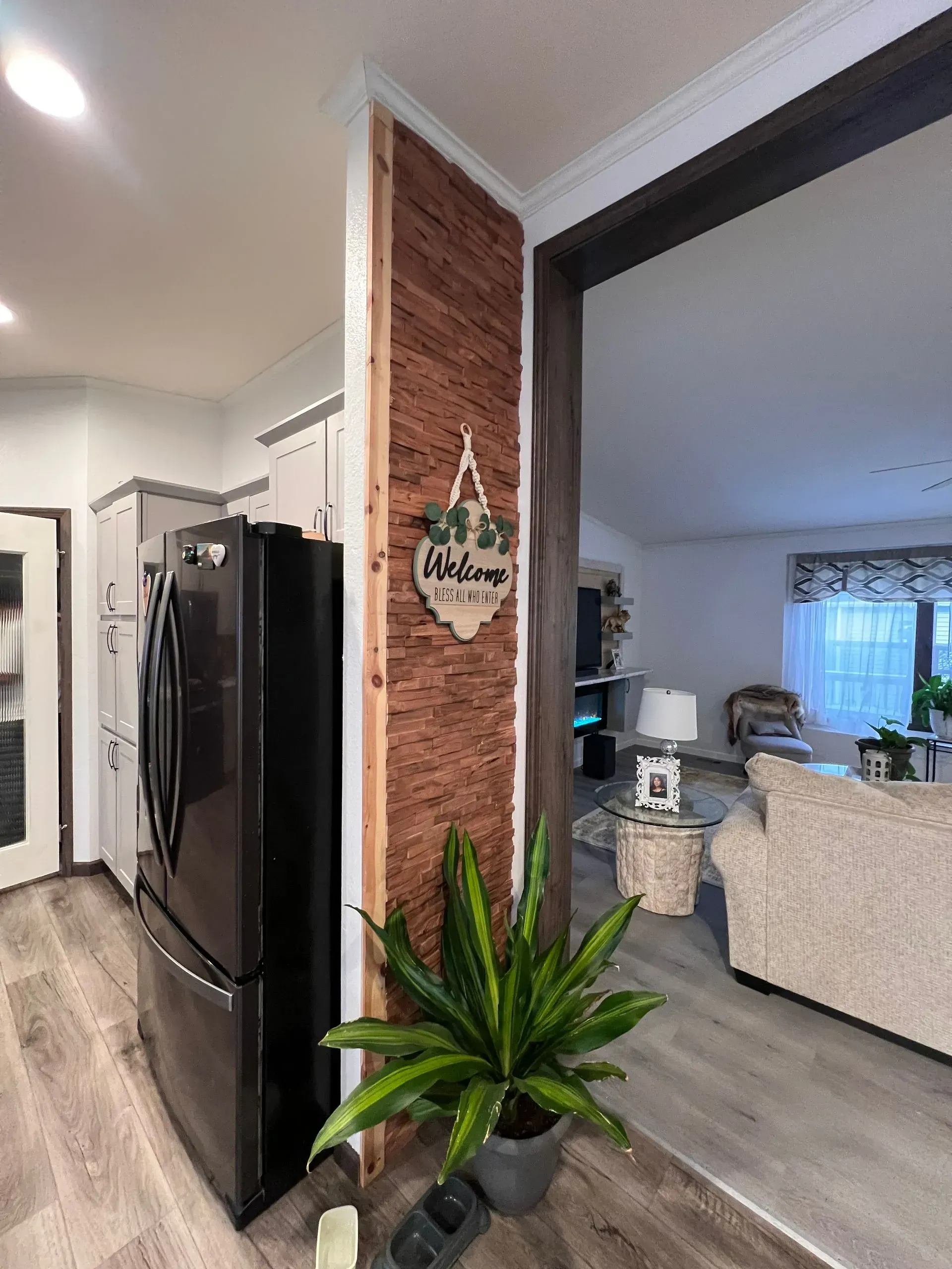 A kitchen with a dark refrigerator, wood-paneled wall, and a living room visible through an archway.