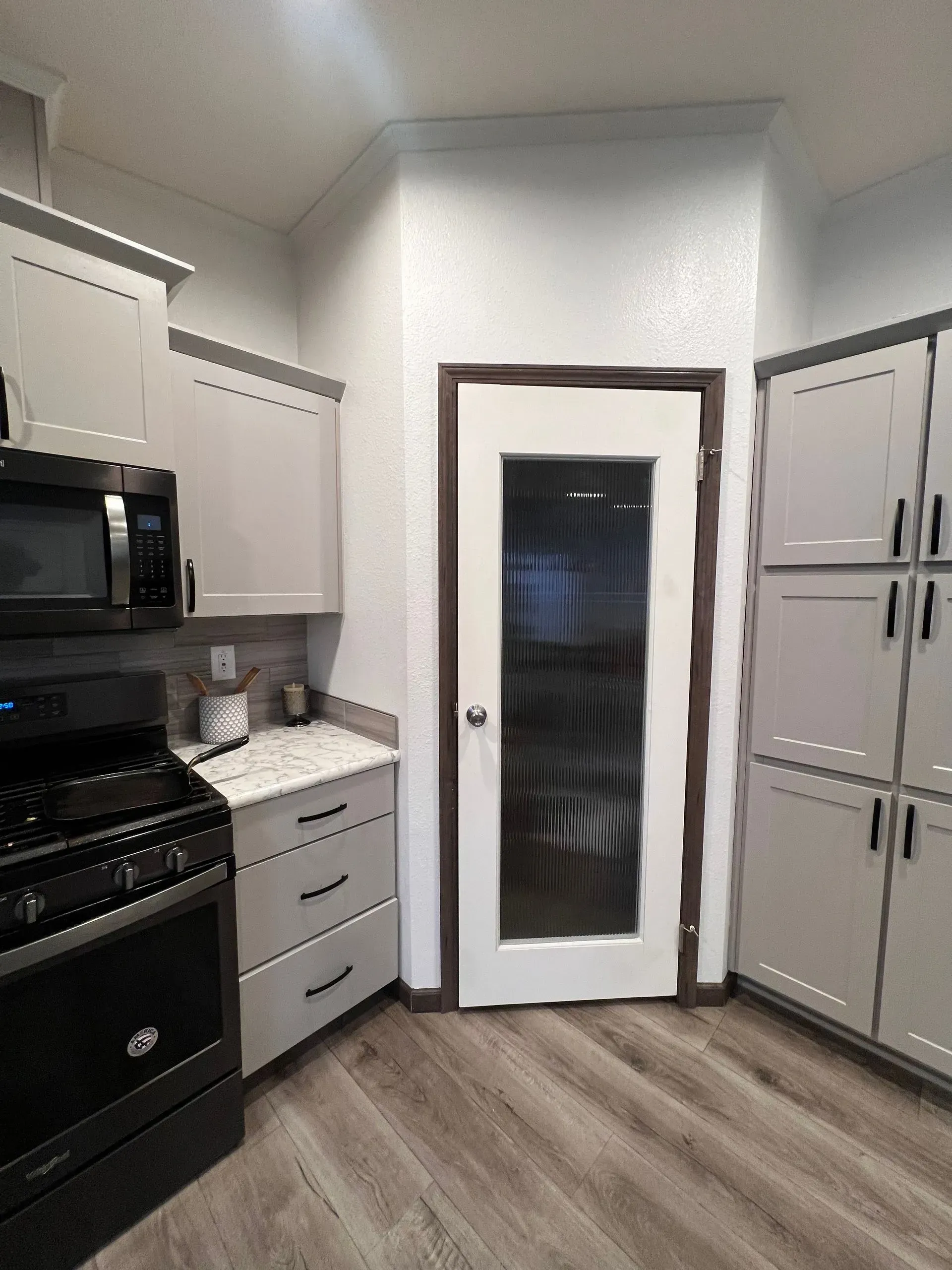 Kitchen with gray cabinets, black appliances, and a glass-paneled door.