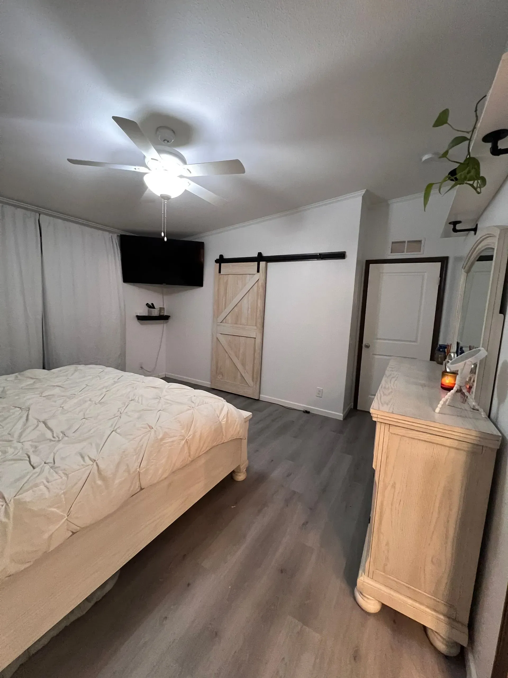 Bedroom with bed, television, sliding door, white dresser, and ceiling fan.