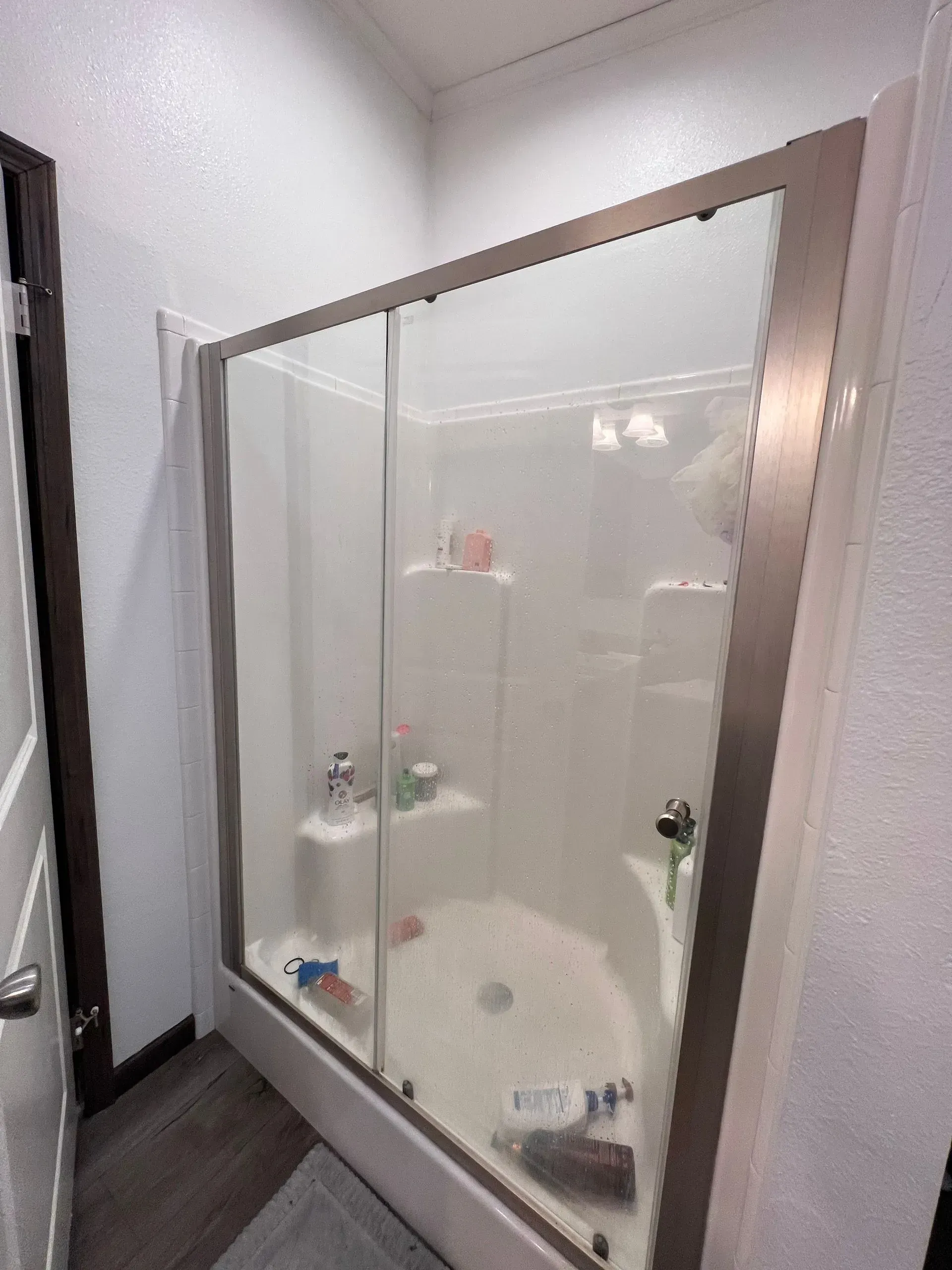 Bathroom with white walls and a shower enclosed by sliding glass doors.