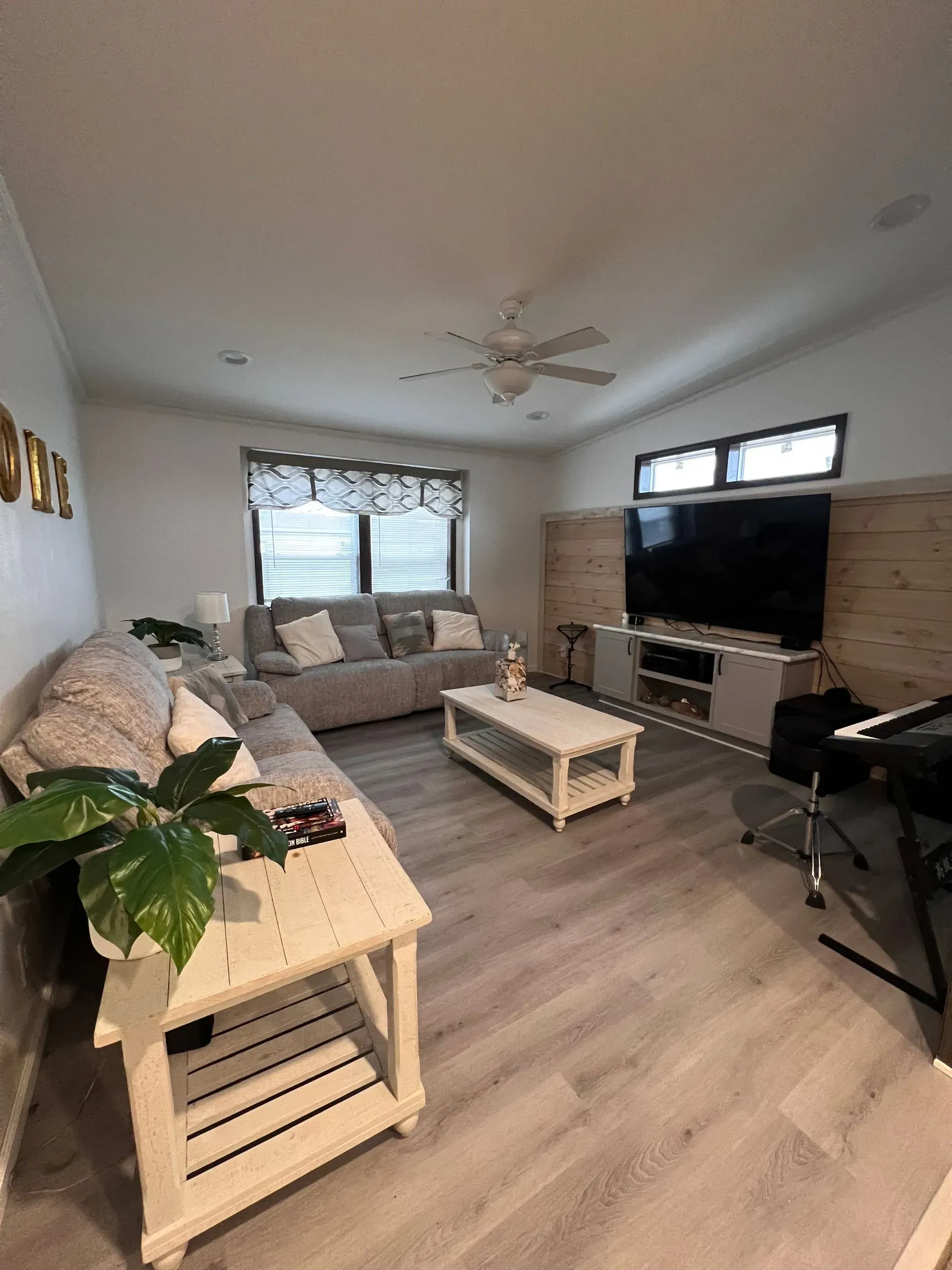 Living room with gray sofa, white coffee table, large TV, and light wood flooring.