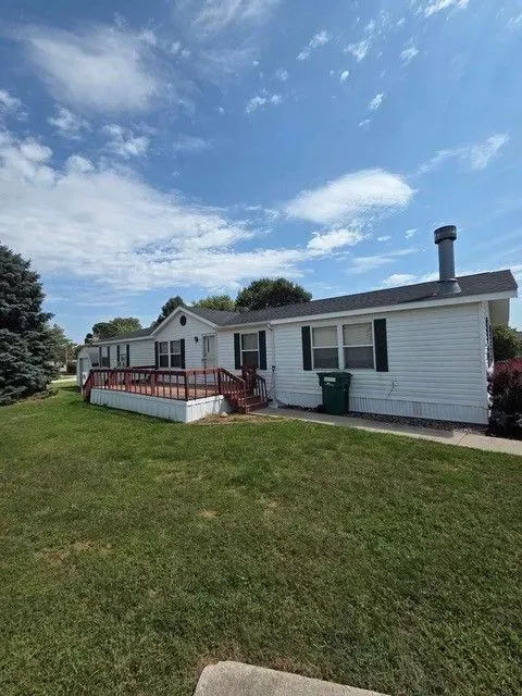 White house with a green lawn, red deck, and a blue sky with clouds.