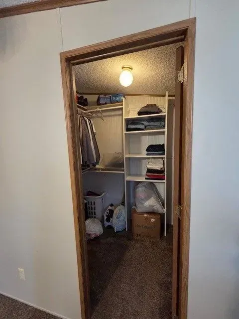 A walk-in closet with brown carpet, clothes on rods, and shelving. White walls and wooden door frame.