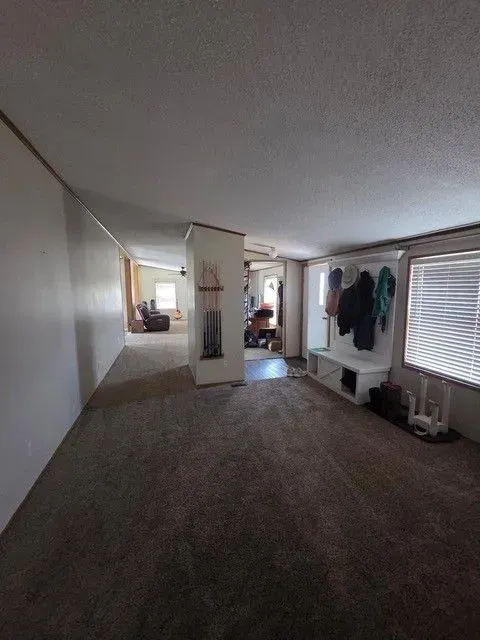 Interior of a house with a carpeted floor. Coats hang on a wall, a wall divides the space.