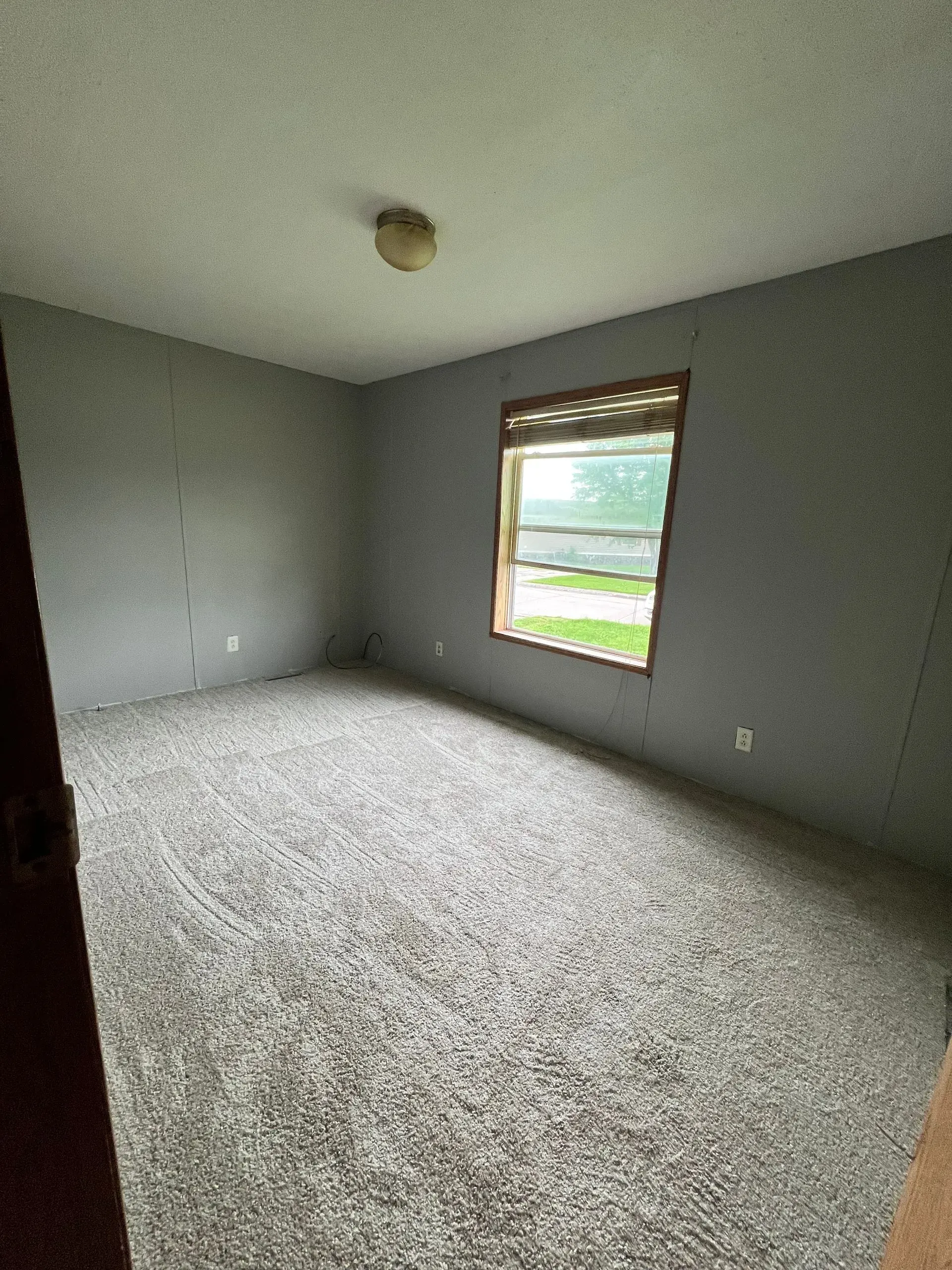 Empty room with gray walls and carpet, a window, and a ceiling light.