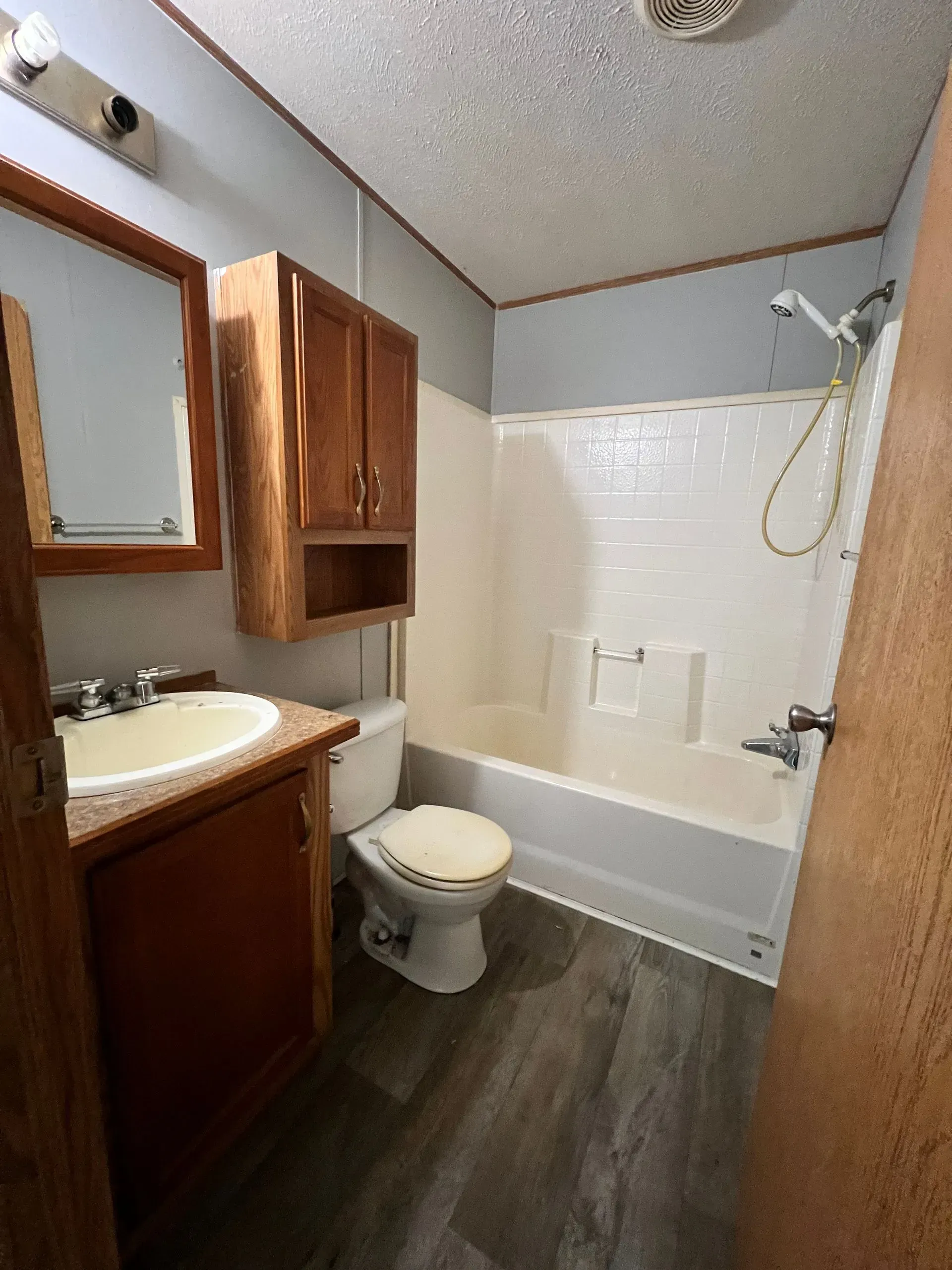 Bathroom with a vanity, toilet, and bathtub/shower. Gray floor, blue walls, and brown cabinets.