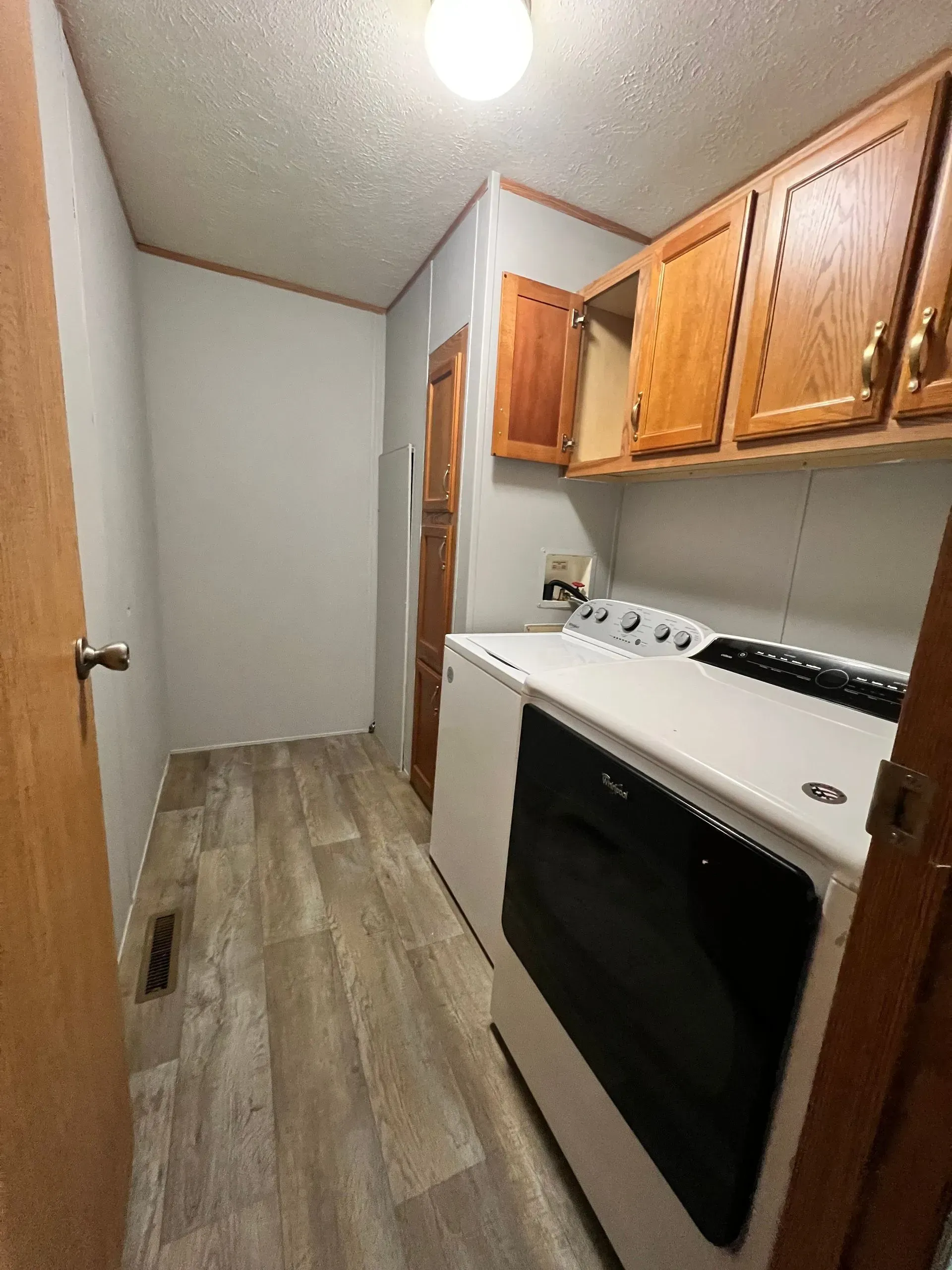 Laundry room with a washing machine, cabinets, and a doorway. Light wood-look flooring and gray walls.