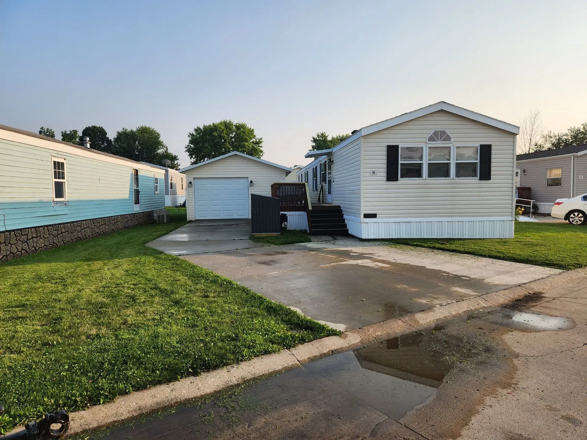 Mobile home with garage, driveway, and lawn. Light blue siding, white trim, and black shutters.