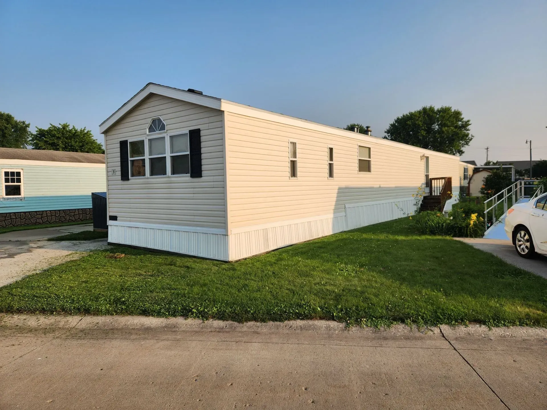 Beige mobile home with white trim and black shutters on a grassy lawn.