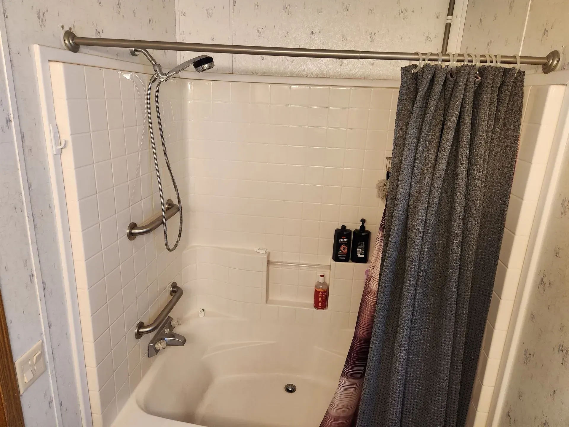 Bathroom shower with a tub, shower head, curtain, and grab bars.