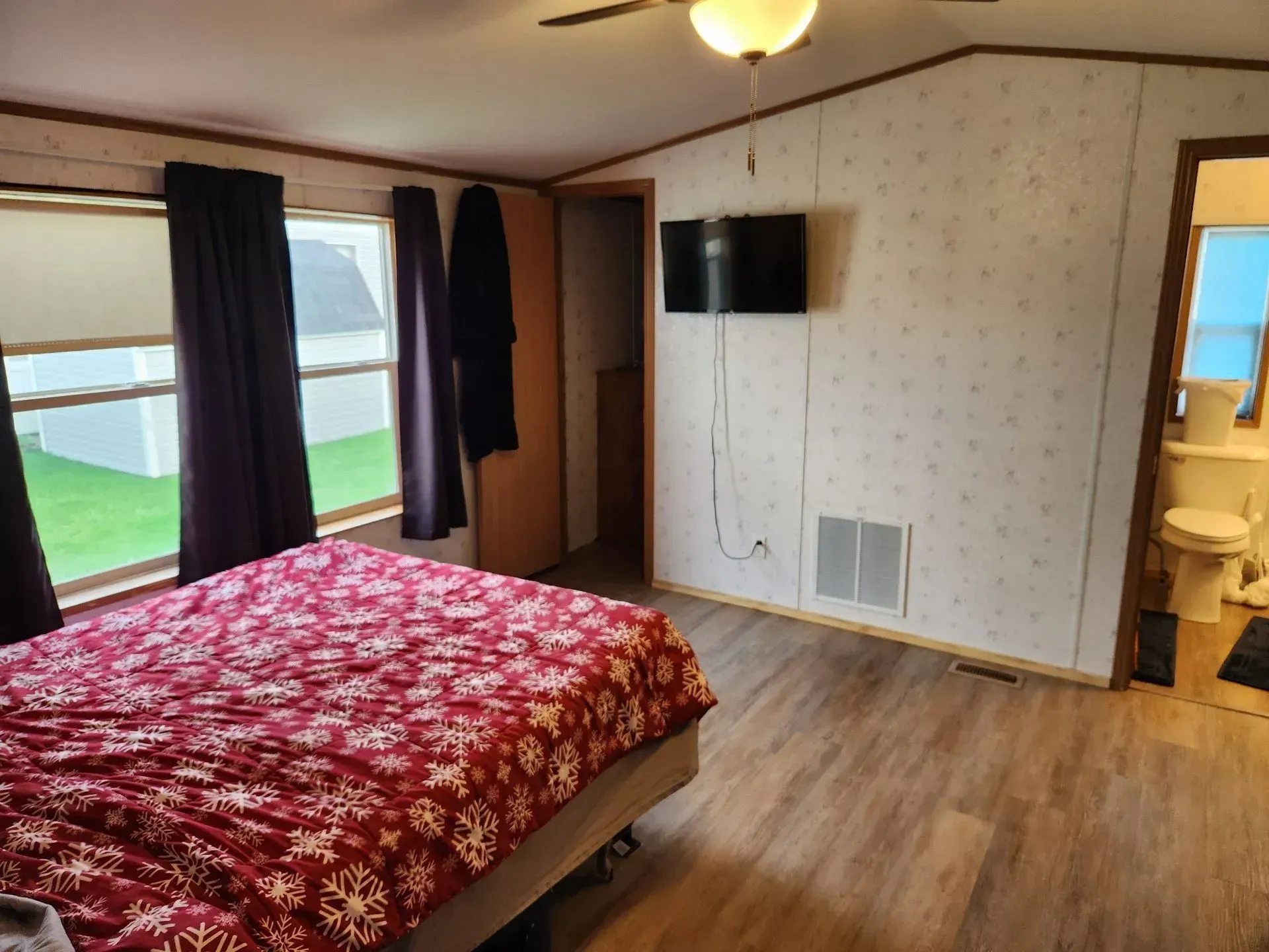 Bedroom with bed, TV, and en-suite bathroom. Red patterned bedspread, wooden floor, and a window.