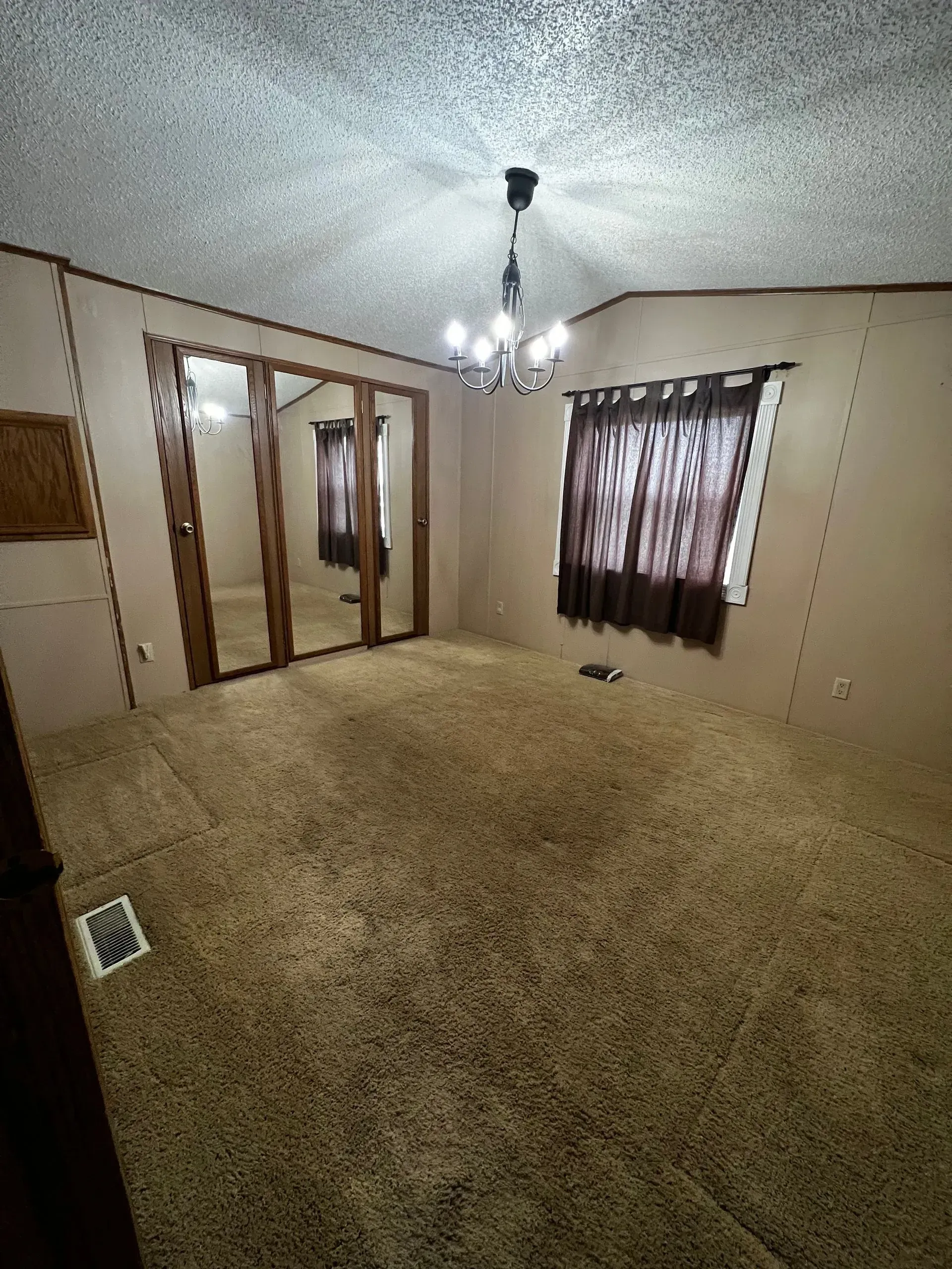Empty room with brown carpet, large mirrored closet doors, and a chandelier.