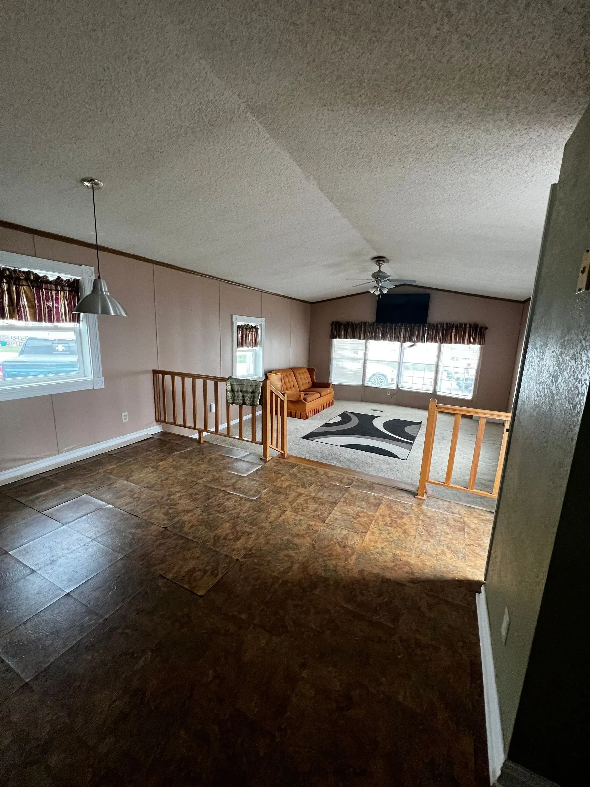 Interior view of a mobile home's living room and dining area, brown panel walls, and wood-like flooring.