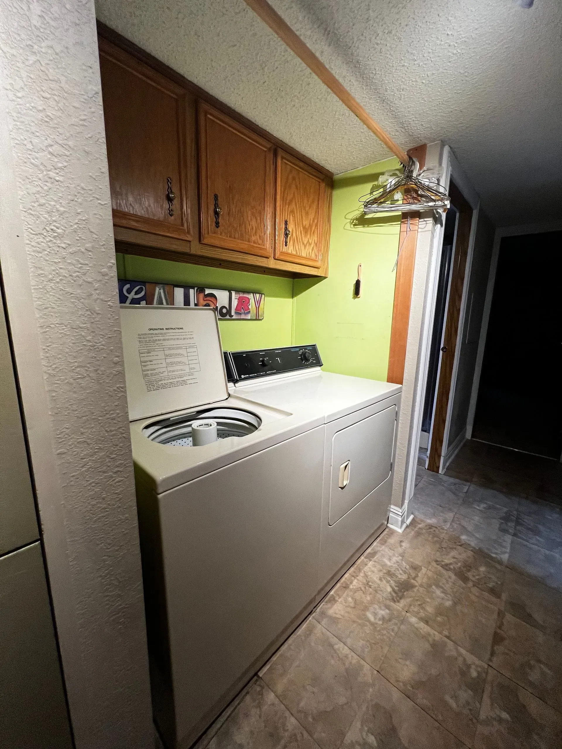 Laundry room with a washing machine, cabinets, and a hallway. Green wall, brown cabinets, and beige floor.