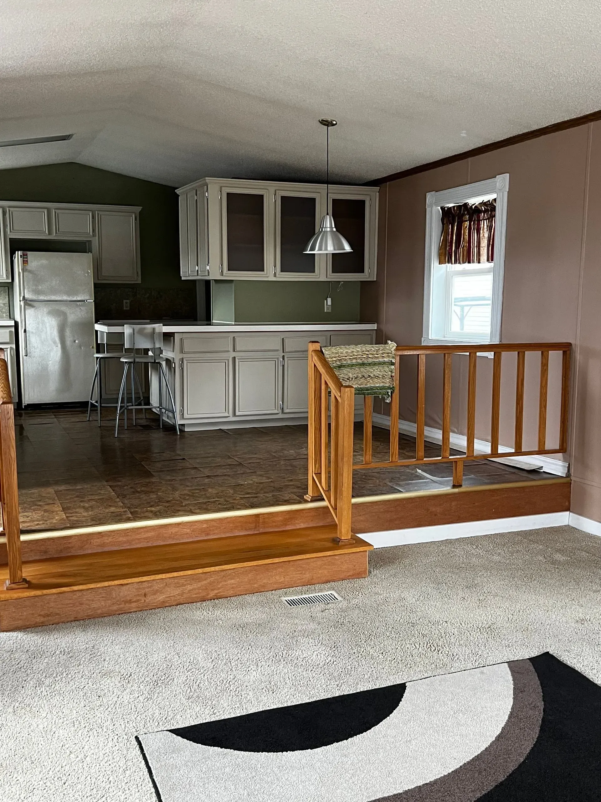Interior view of a kitchen with light-colored cabinets, a small window, and a wood-railed step up.